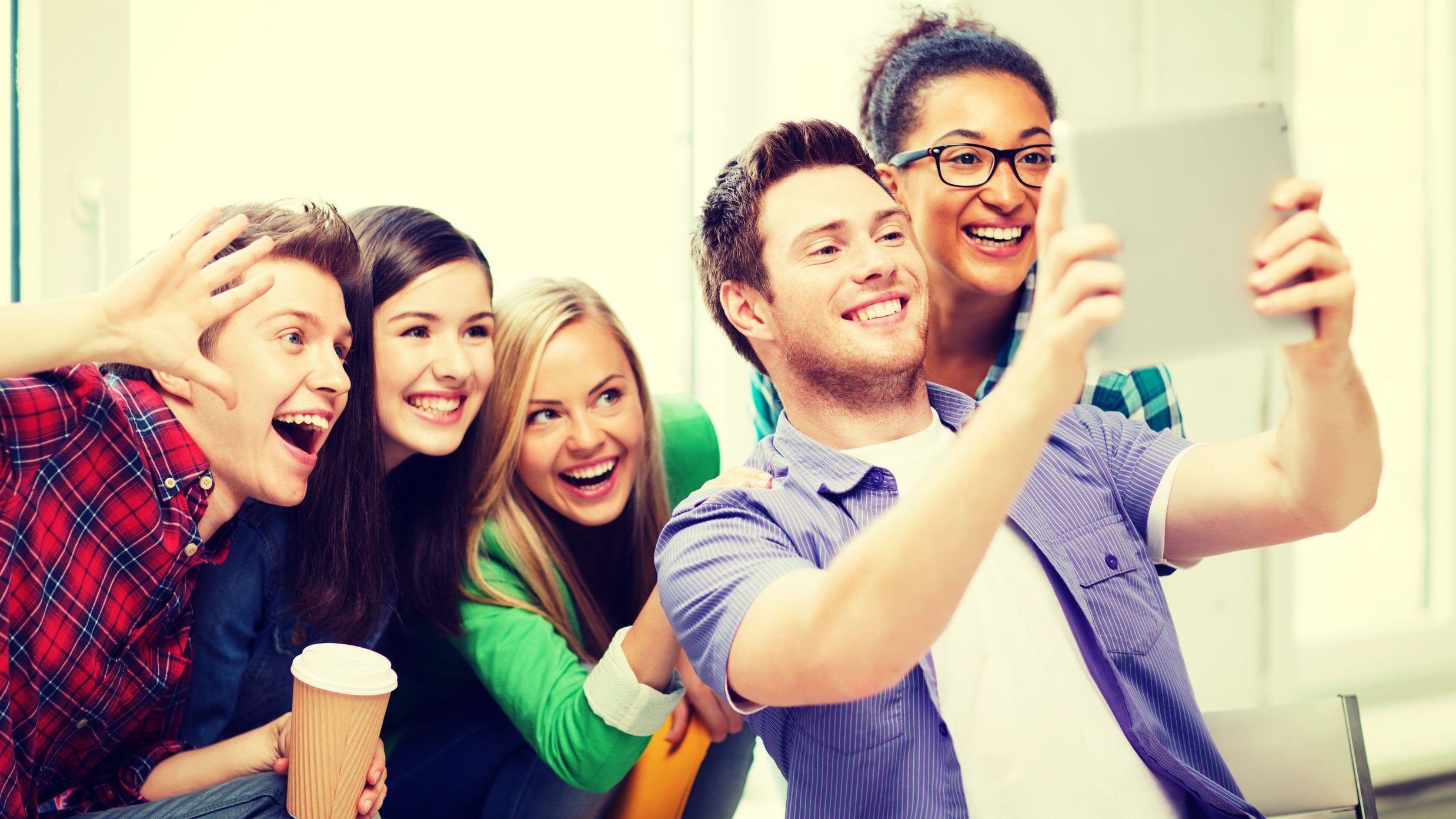 Grupo de amigos posando para uma selfie que o homem da frente irá tirar com um tablet.