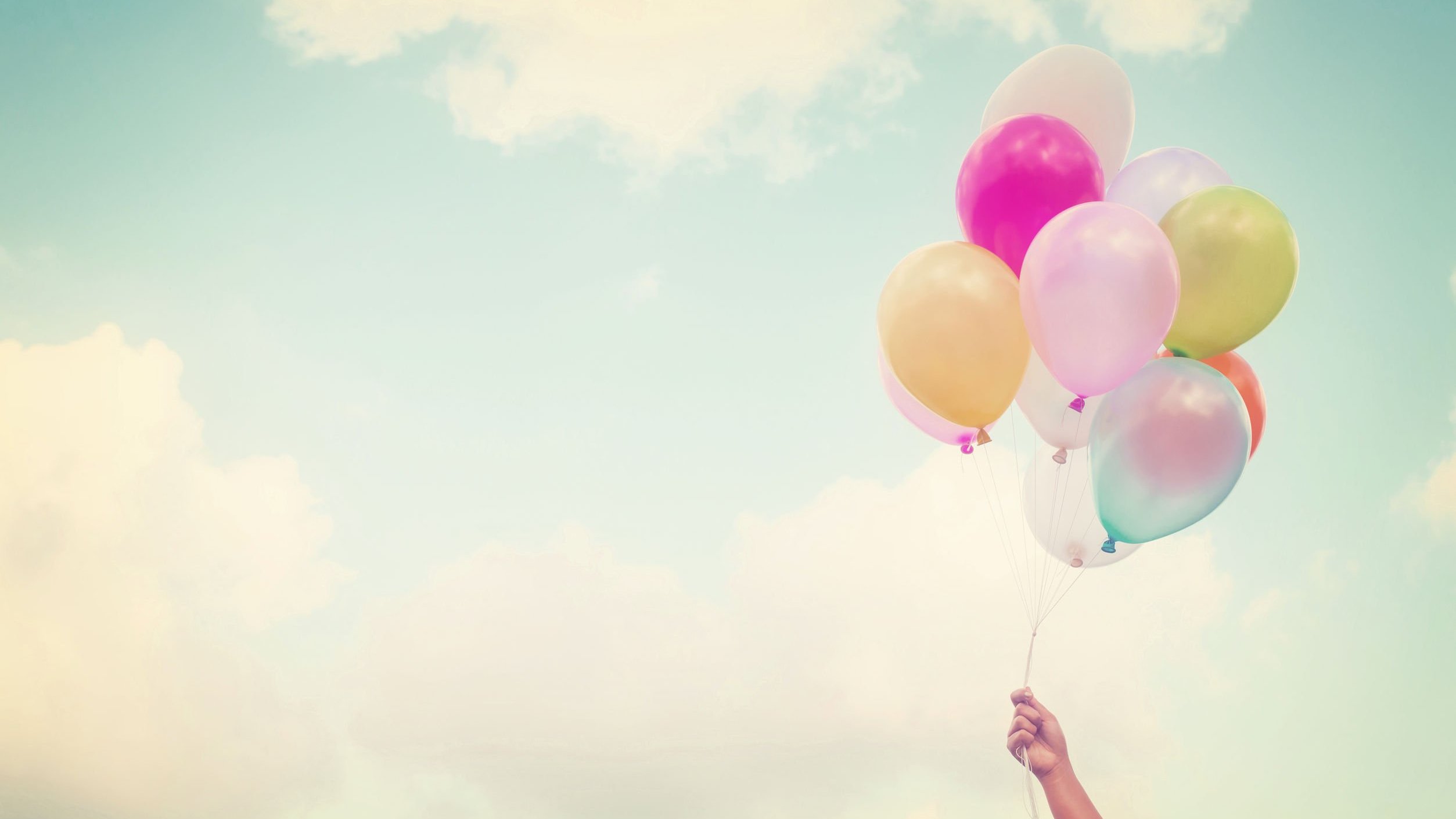 Mão segurando balões coloridos com céu ao fundo