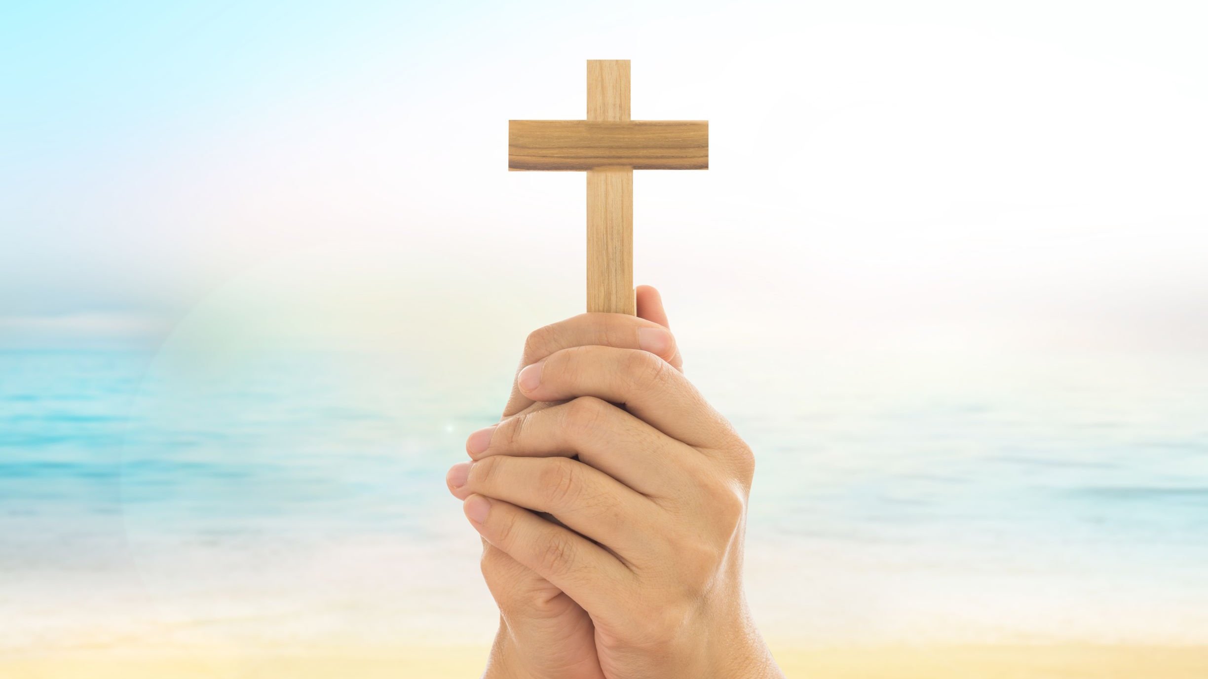 Mãos segurando uma cruz em frente ao mar.