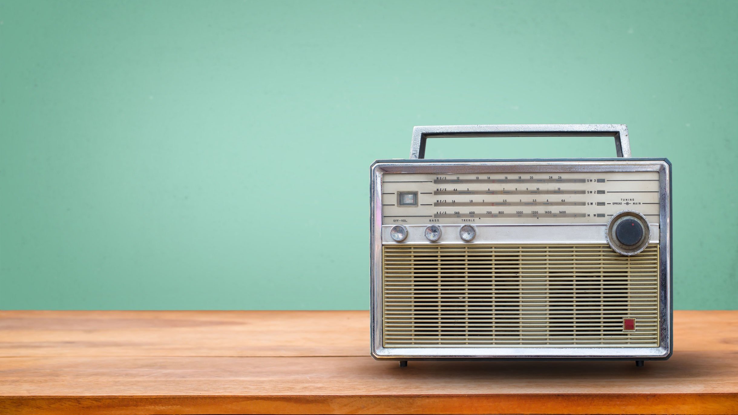 Rádio antigo com alça em cima de móvel de madeira.