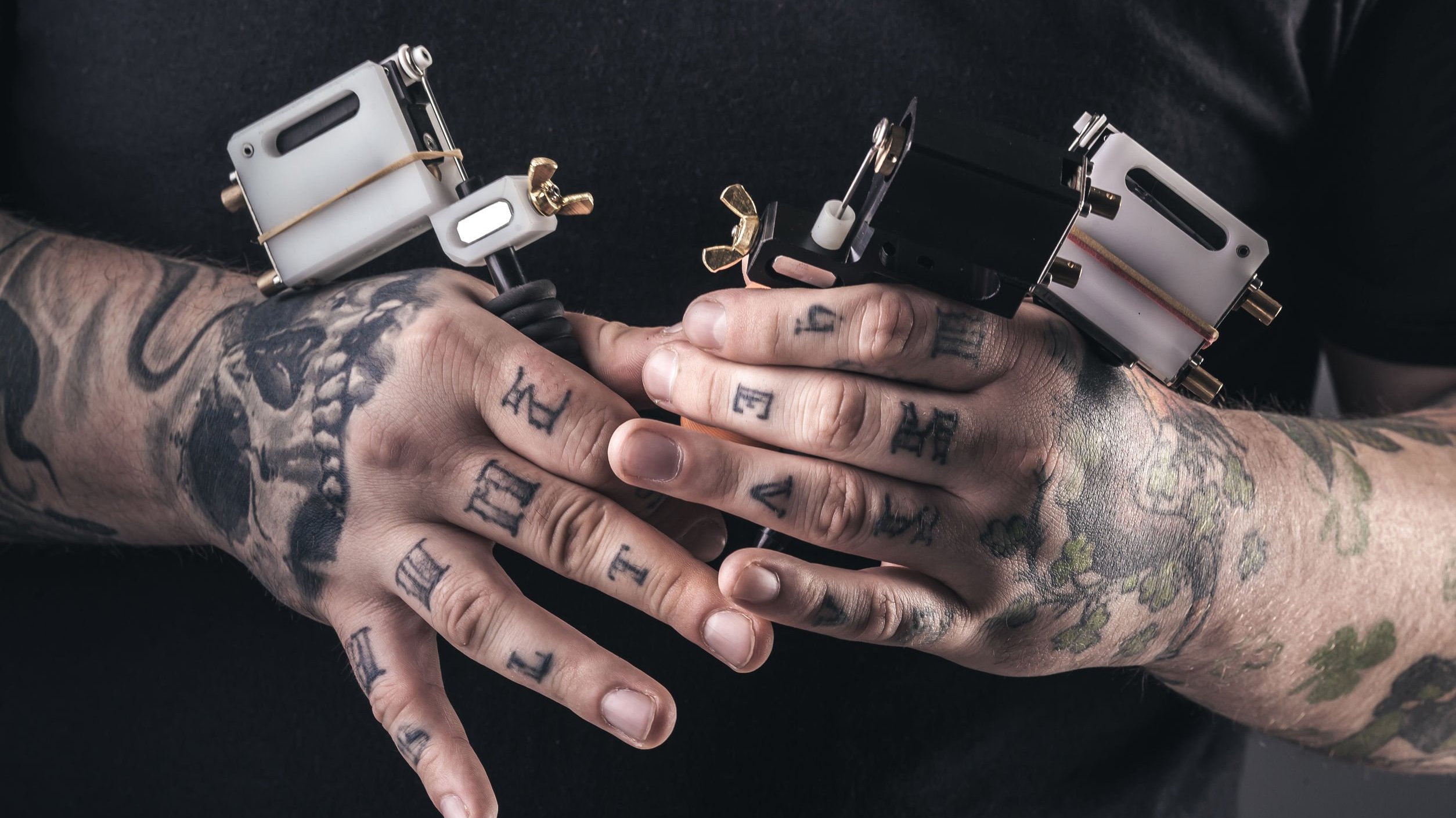 Mãos tatuadas segurando aparelhos de tatuagem.
