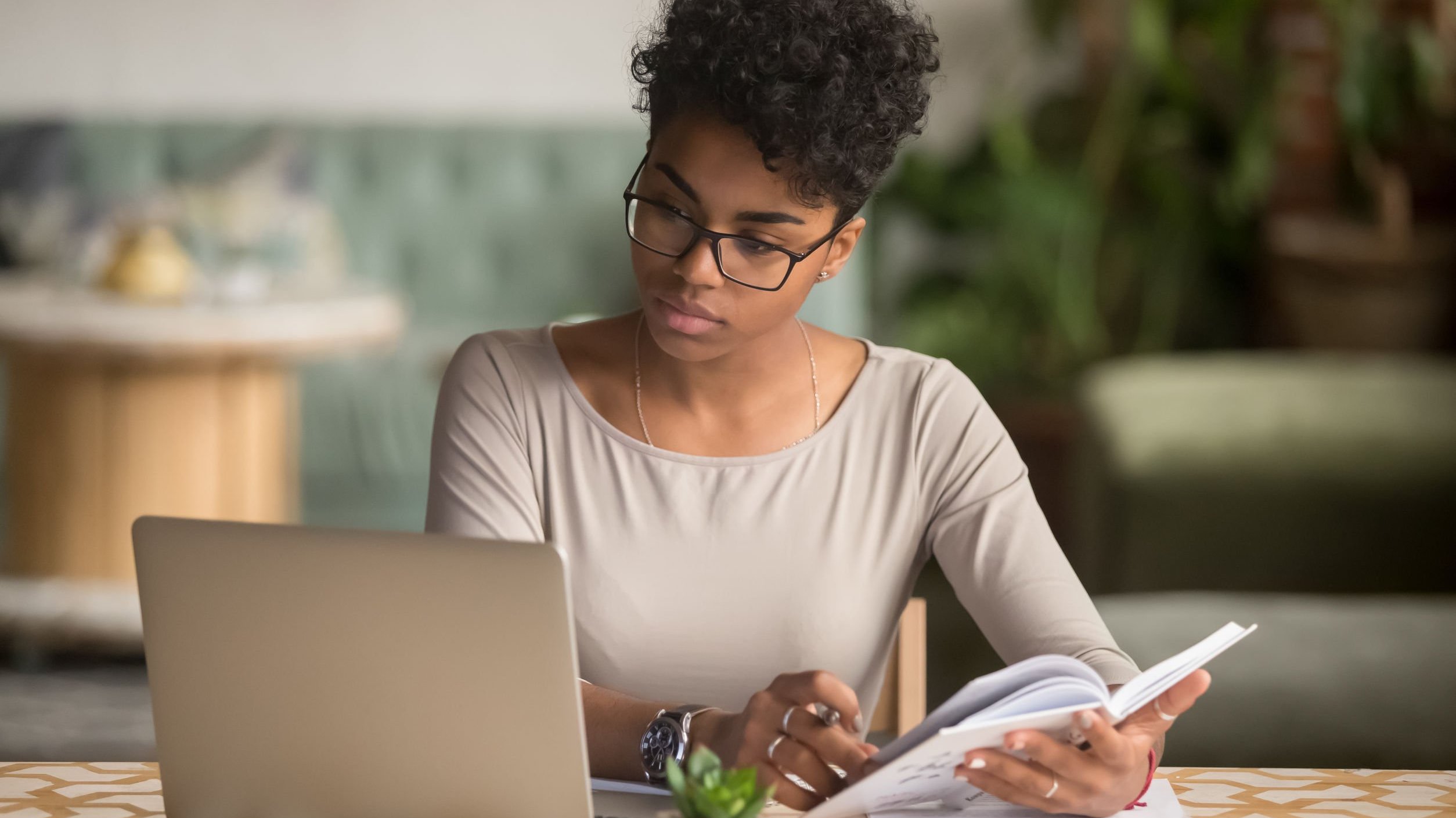 Mulher olhando para o computador e segurando um livro