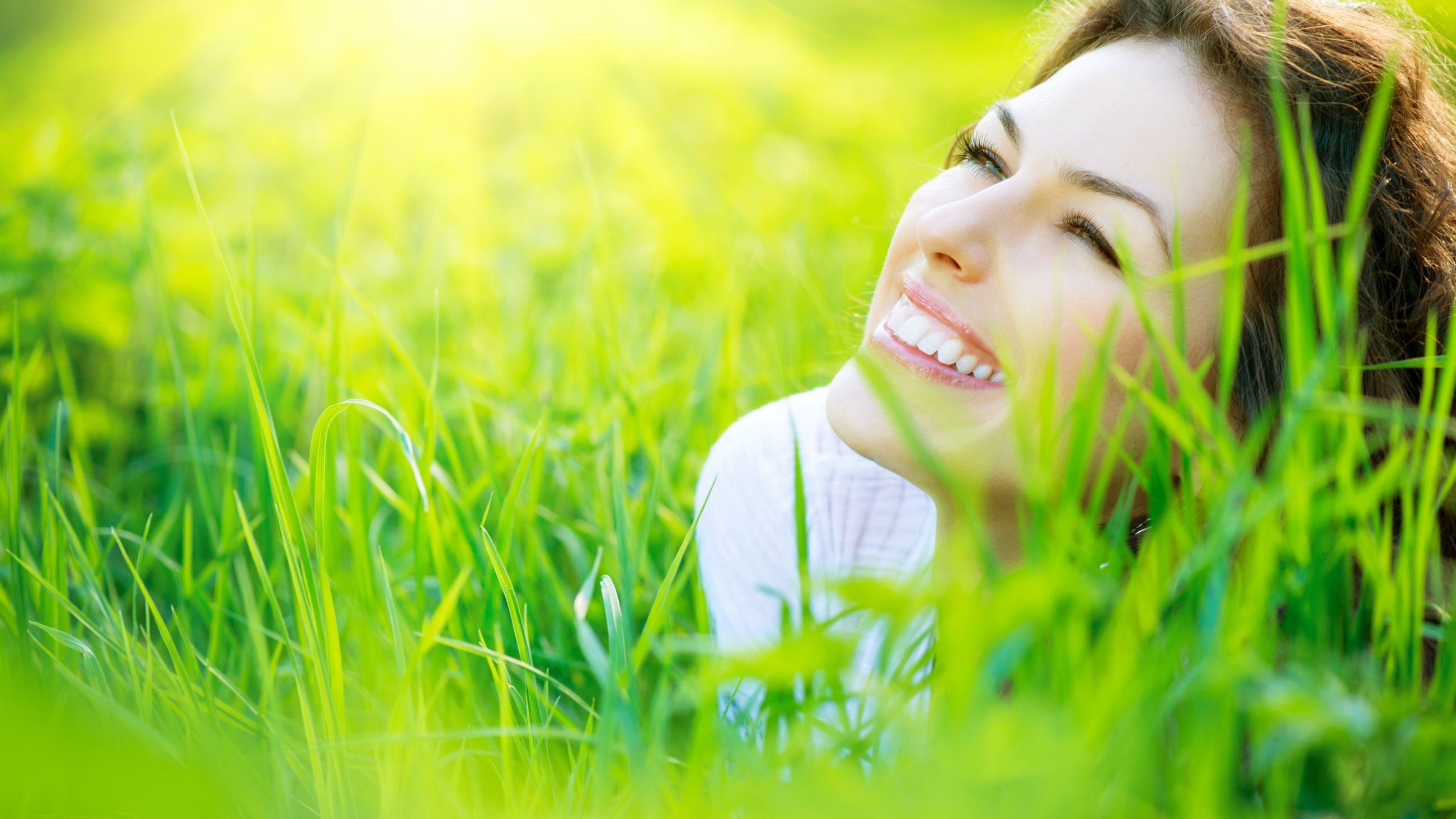 Mulher deita de bruços na grama e sorrindo.
