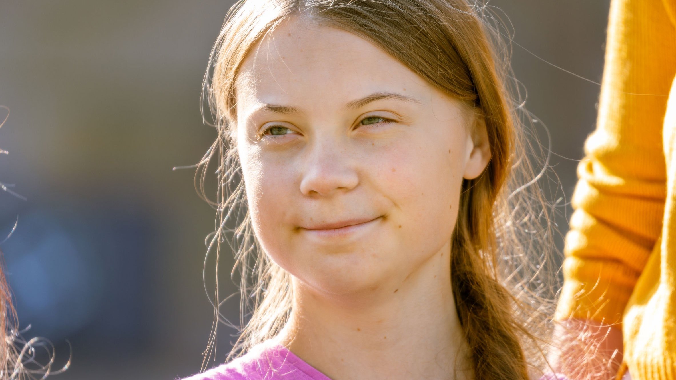 Greta Thunberg sorrindo, olhando para sua diagonal direita.