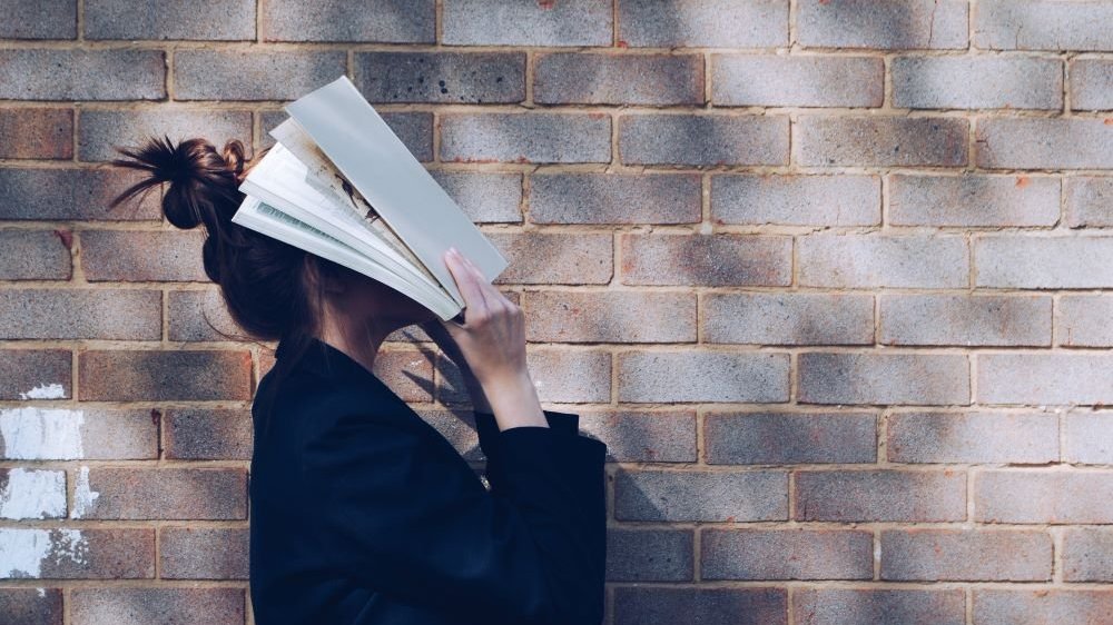 Mulher segurando um livro aberto sobre seu rosto.