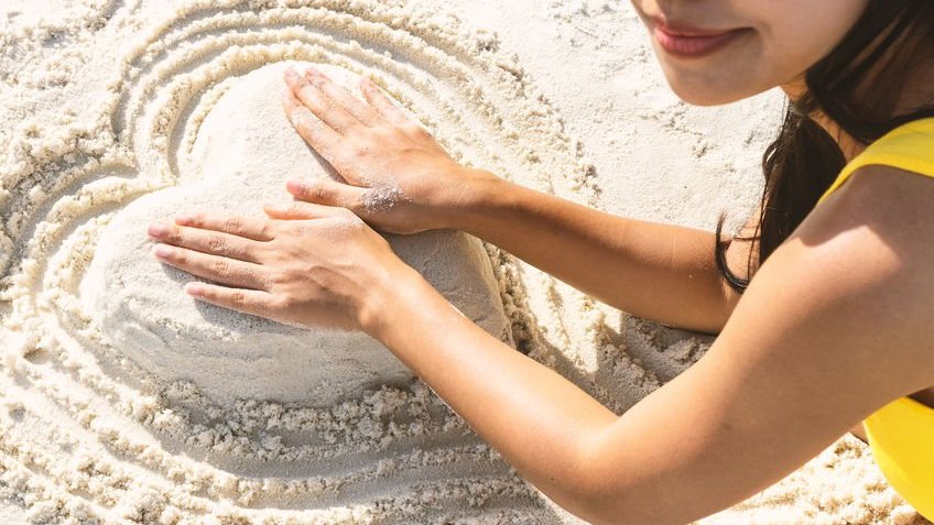 Mulher fazendo coração de areia
