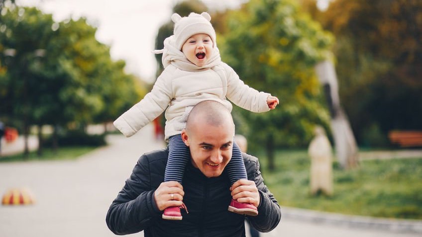 Pai segurando filha sorridente nos ombros