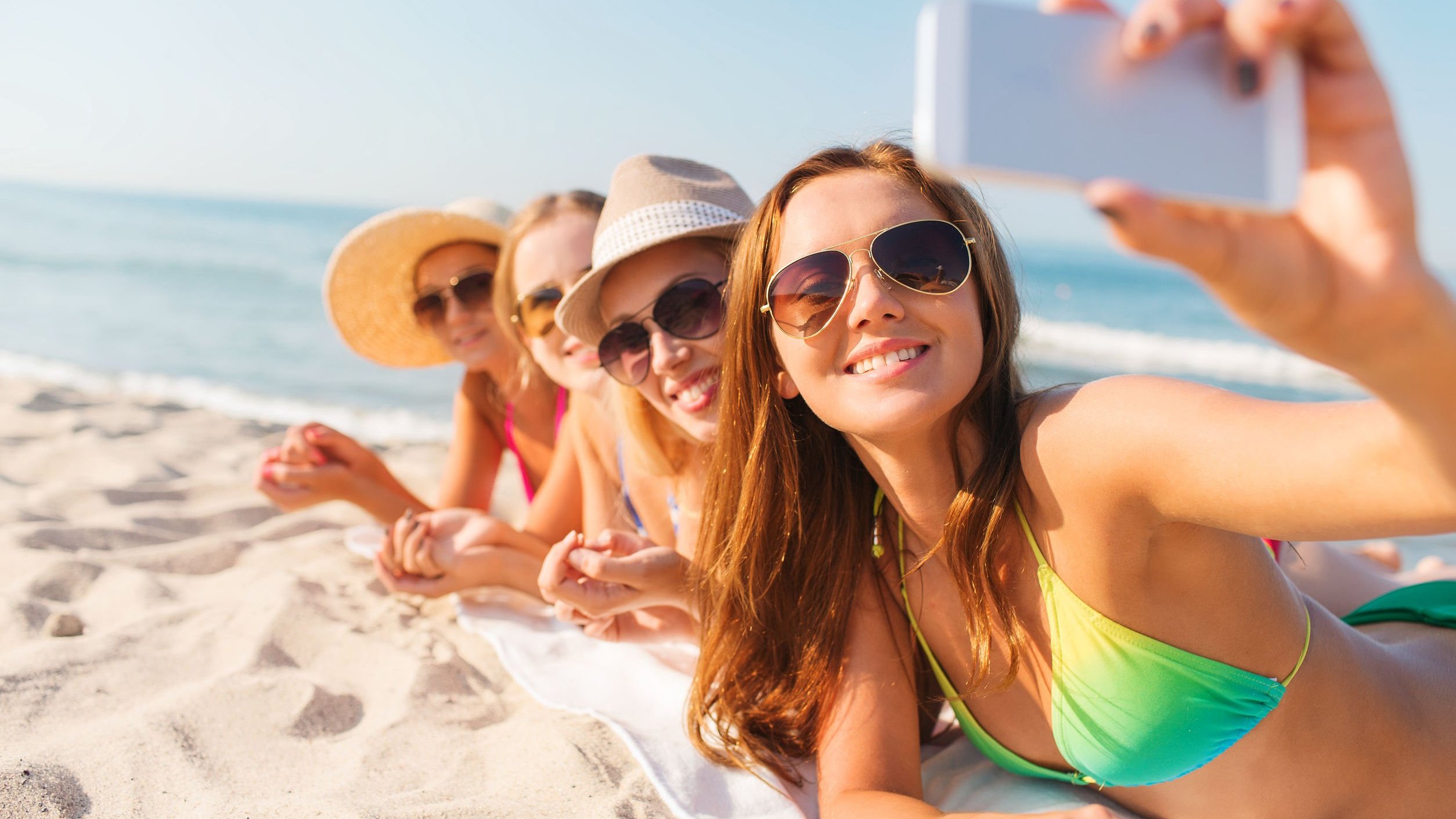 Foto de mulheres deitadas na areia tirando selfie