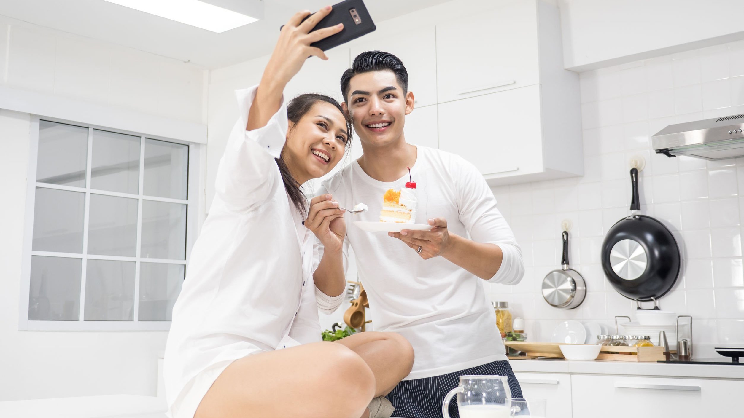 Homem e mulher em casa comendo bolo de aniversário e tirando fotos.