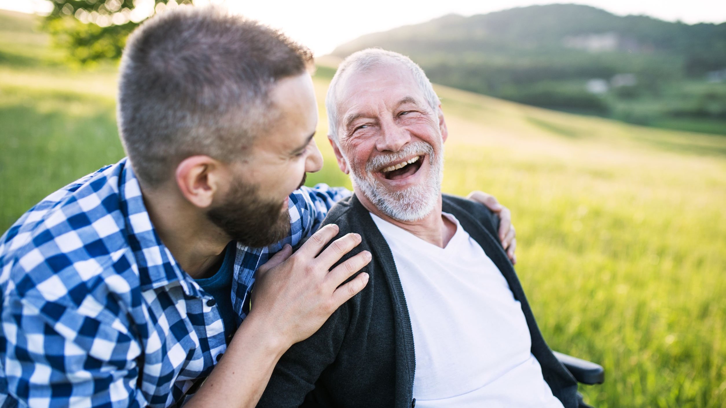 Dois homens sorrindo sentados na grama.