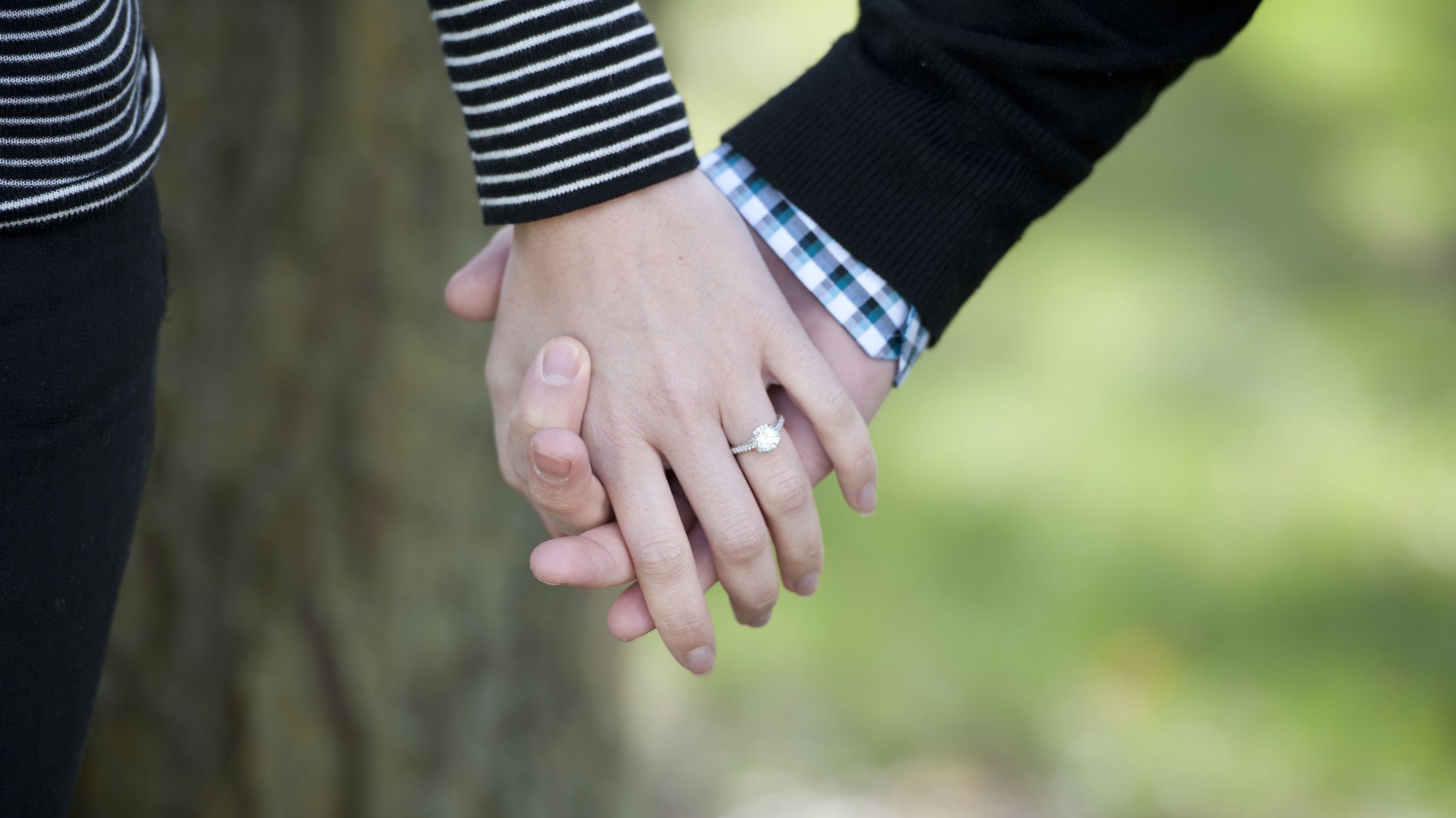 Duas pessoas de mãos dadas, e uma delas usa um anel de noivado.
