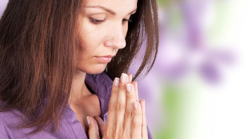 Mulher com mãos em frente ao rosto rezando