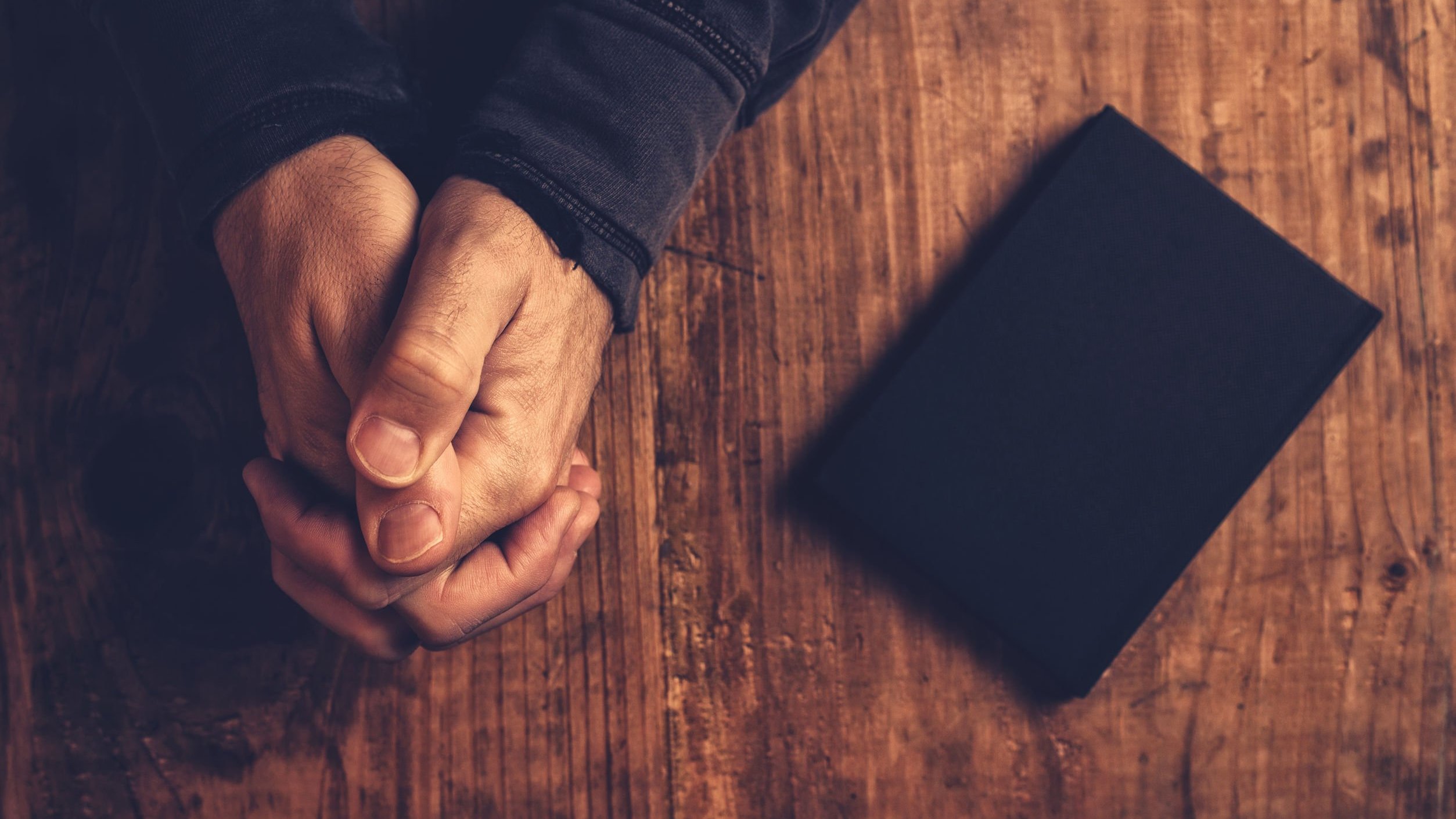 Mãos brancas rezando ao lado de uma bíblia.