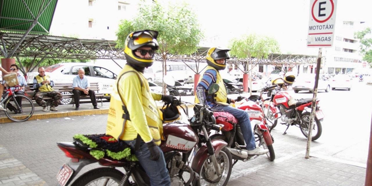 Dois homens vestidos de mototaxistas, sentados em cima de moto na rua