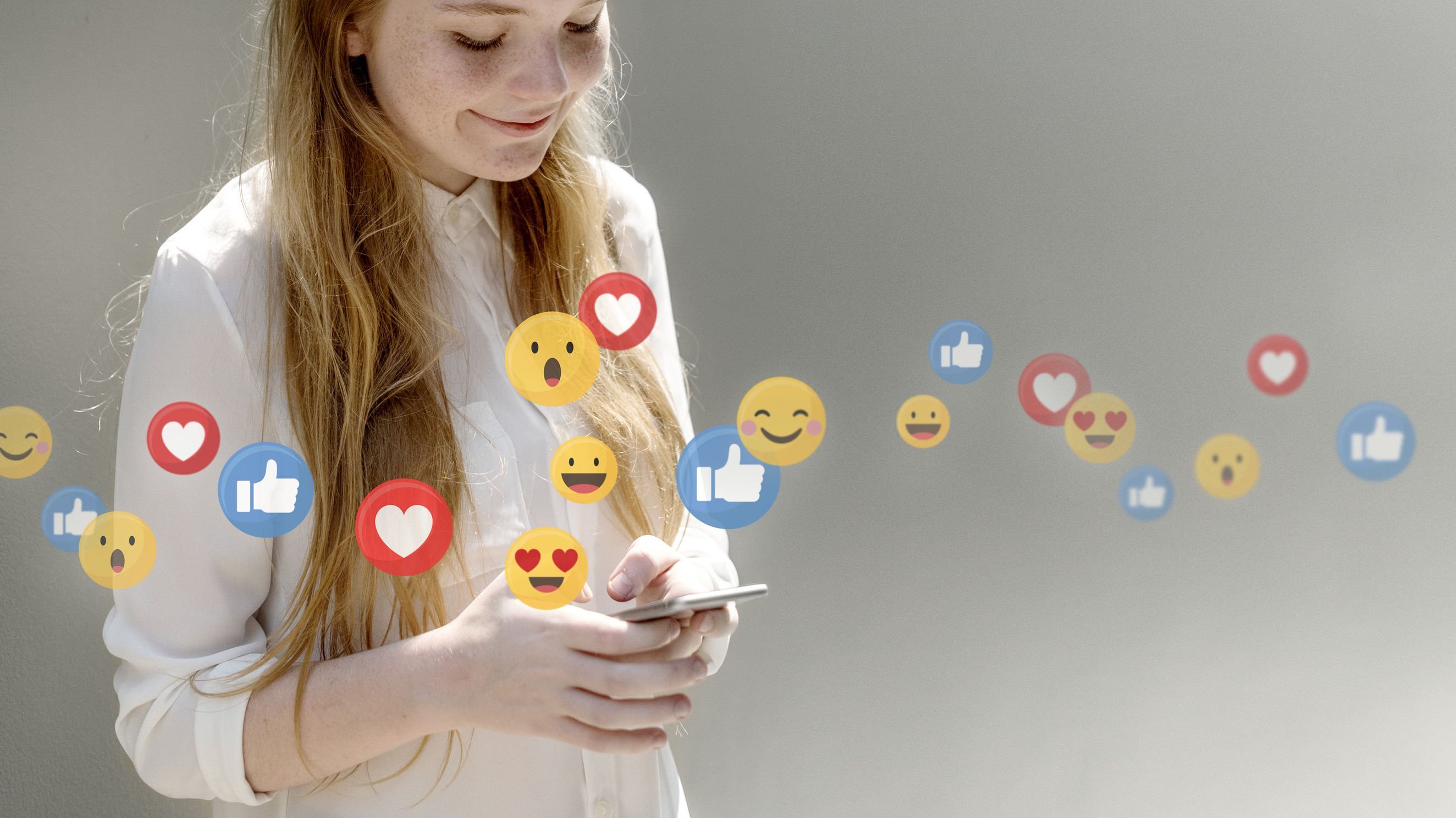 Menina sorrindo para o celular com emojis ilustrados sobre a foto.
