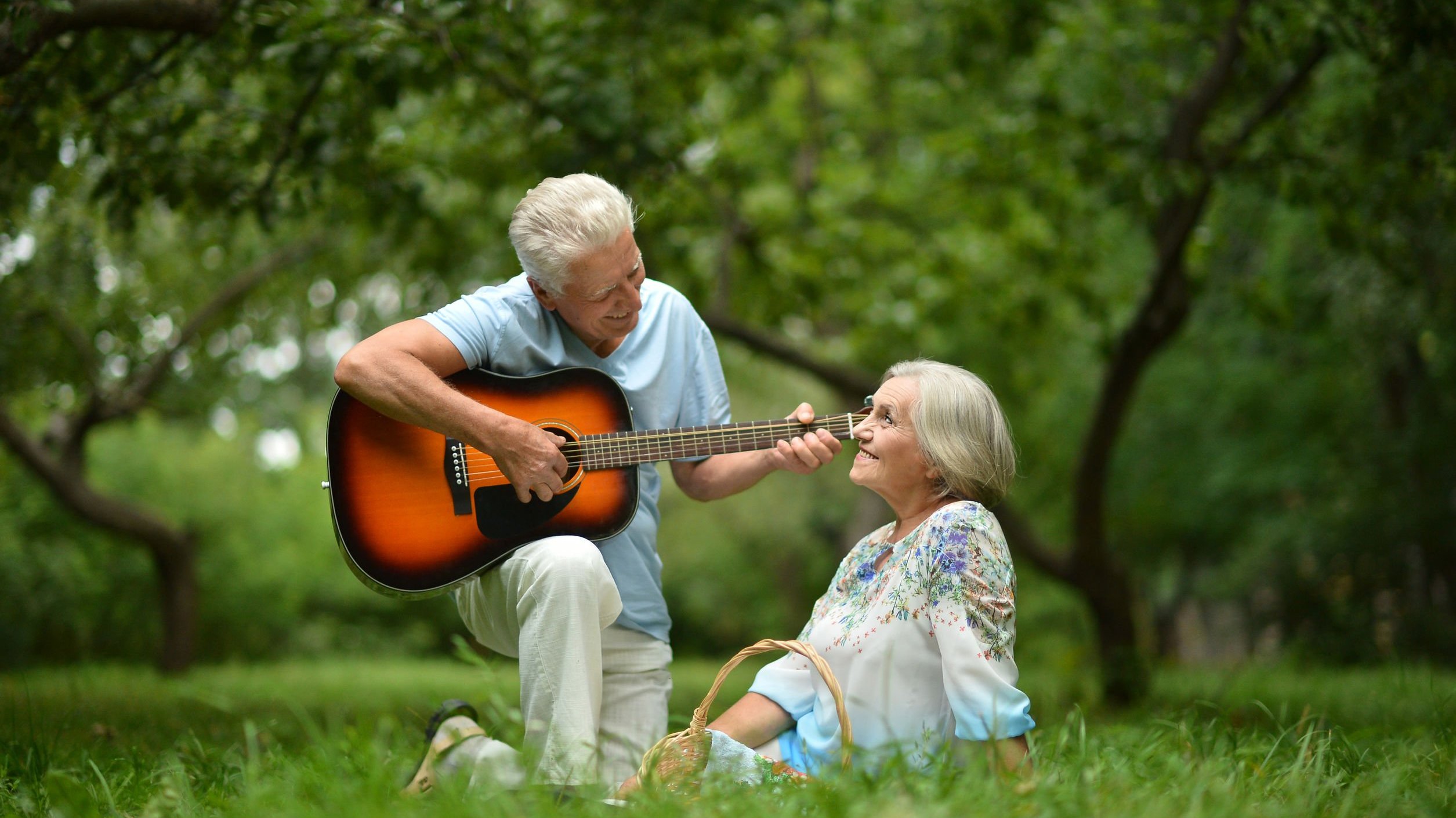 Foto de homem tocando violão e mulher sentada ouvindo