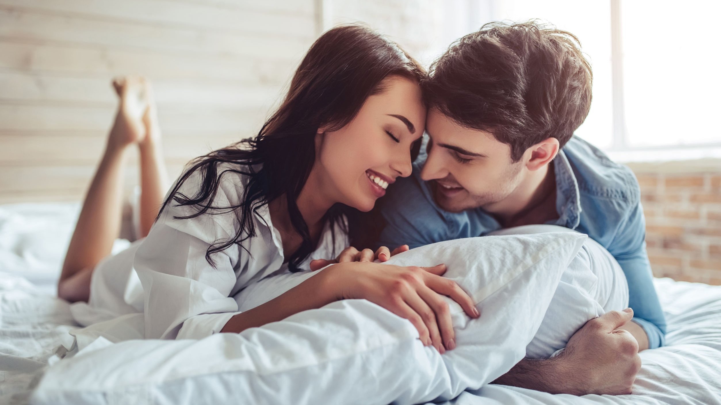 Foto de homem e mulher sorrindo deitados em cama