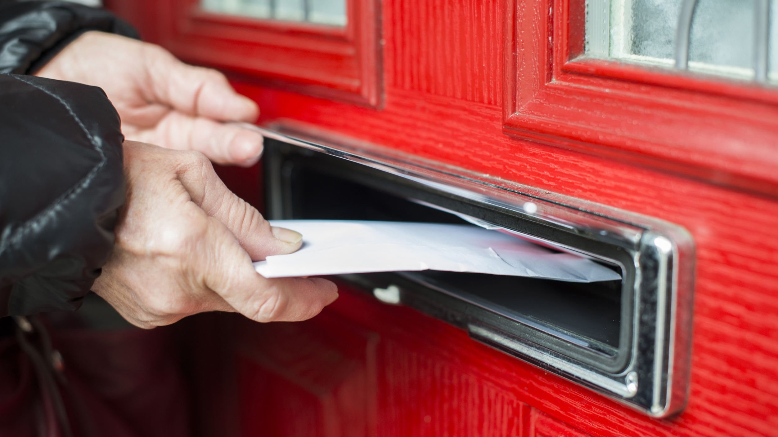 Pessoa colocando uma carta em abertura específica para tal em uma porta.