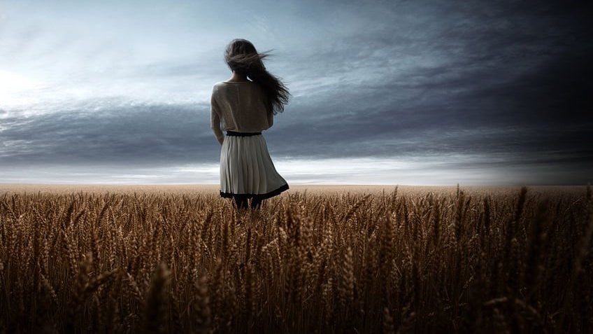 Menina de costas e cabelos ao vento em campo de trigo