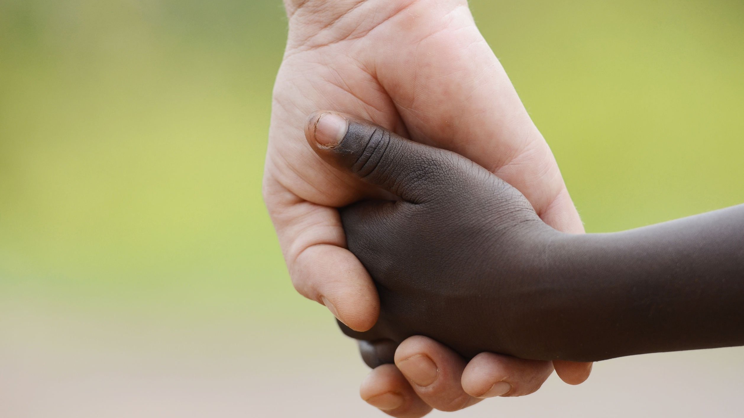 Mão branca de adulta segurando mão de criança negra