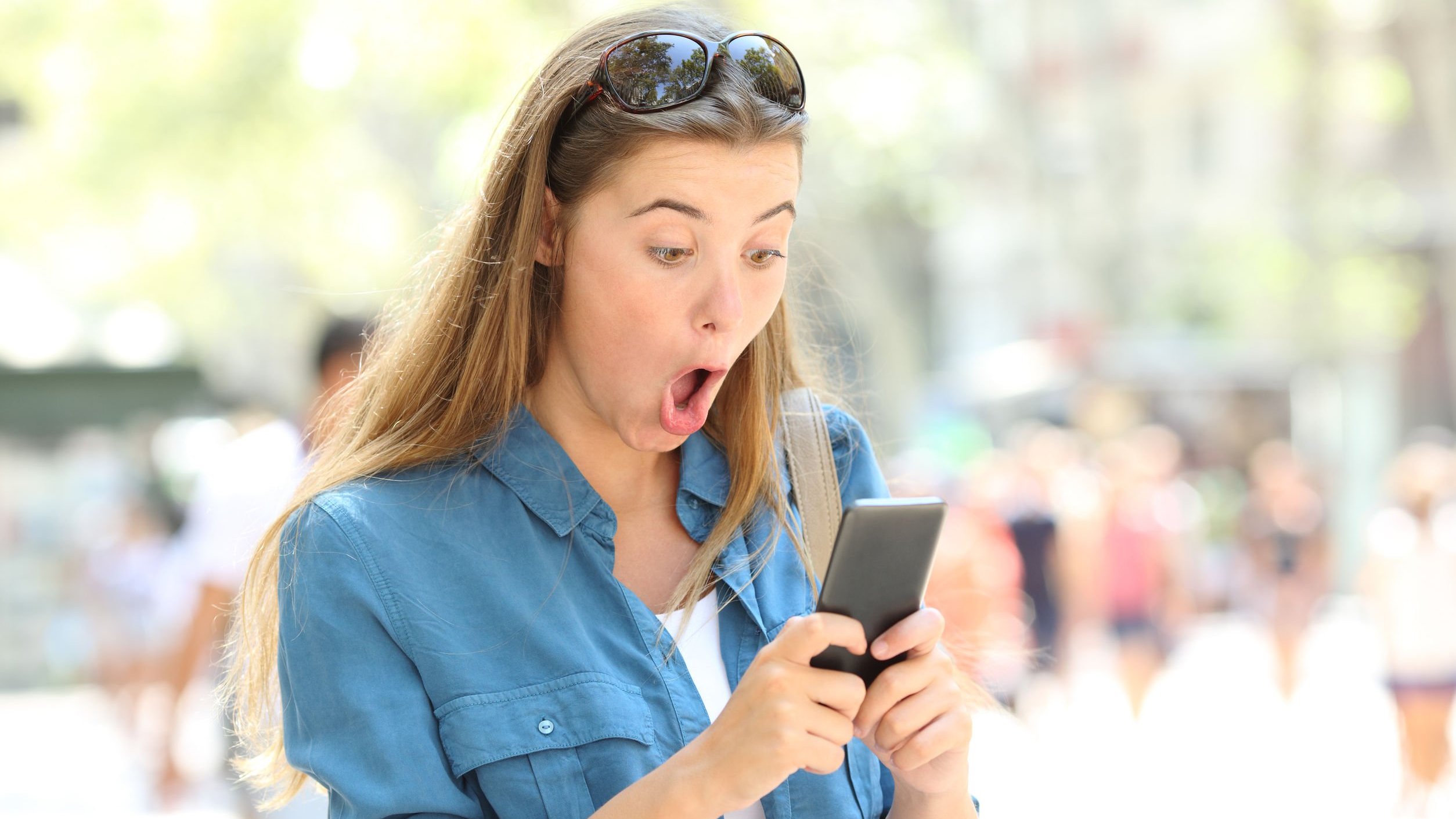 Mulher mexendo em celular com cara de espanto