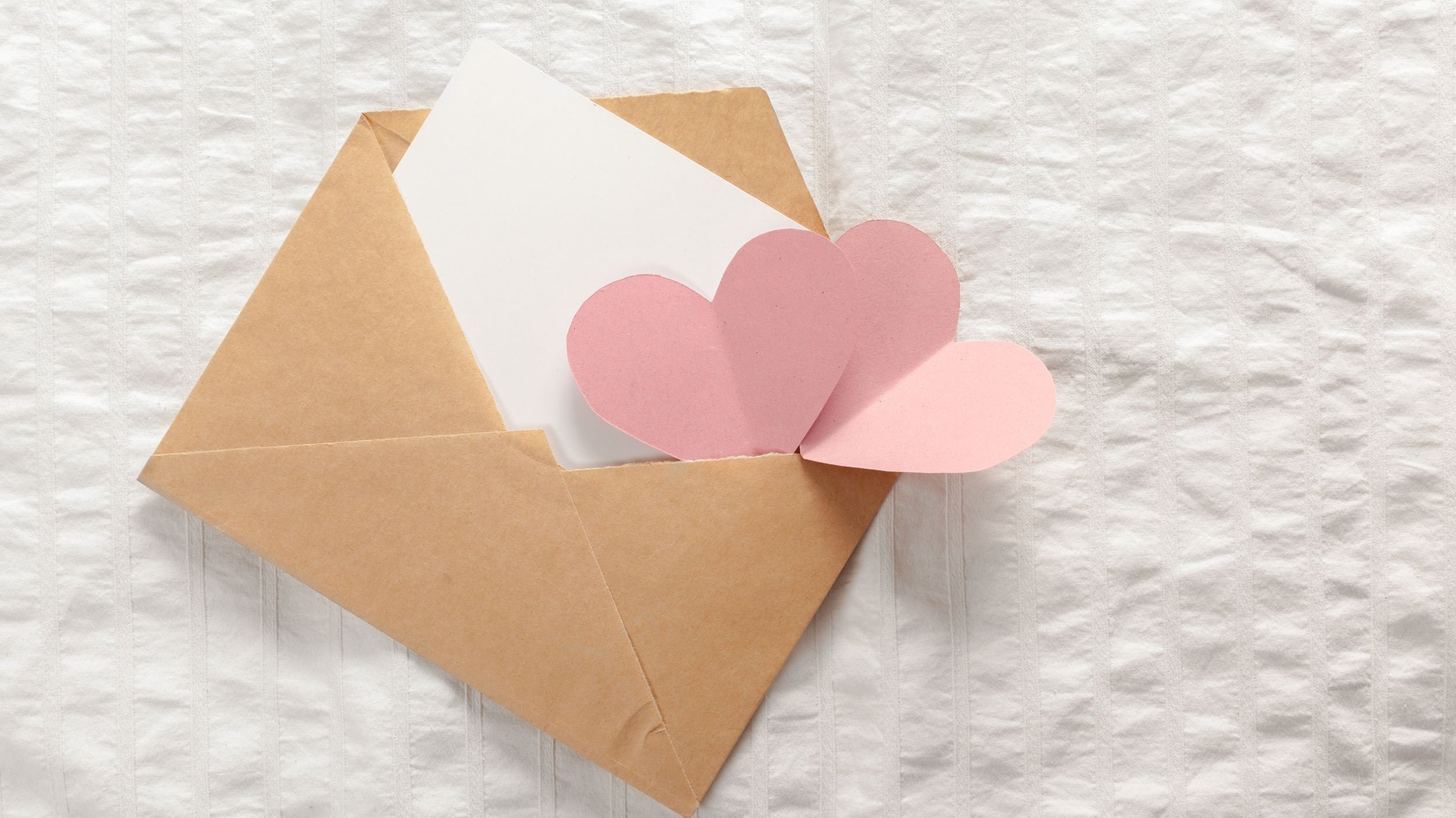 123RF Envelope marrom aberto com carta branca e corações rosa claro saindo de dentro dele.