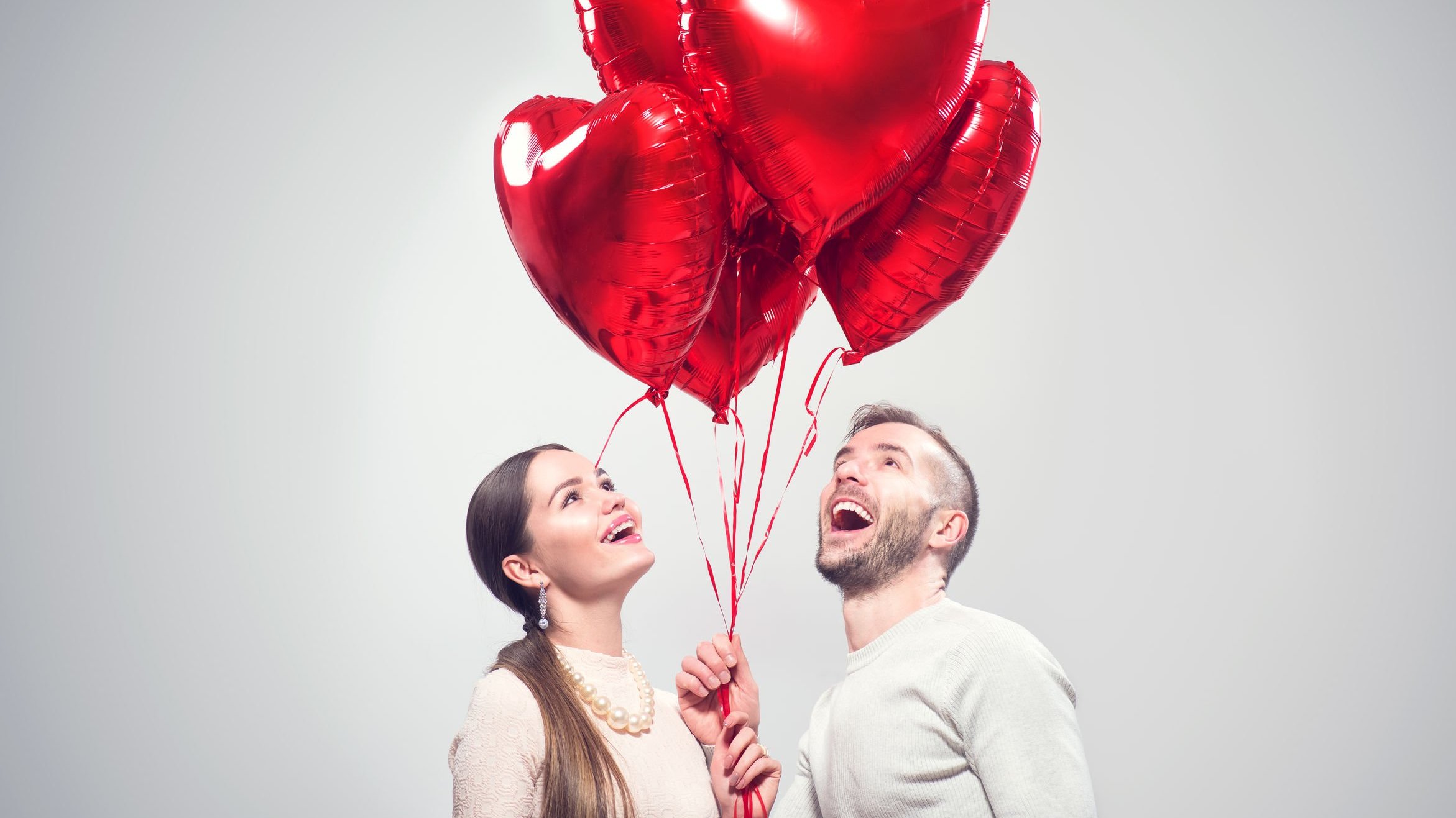 Homem e mulher seguram balões vermelhos em formato de coração