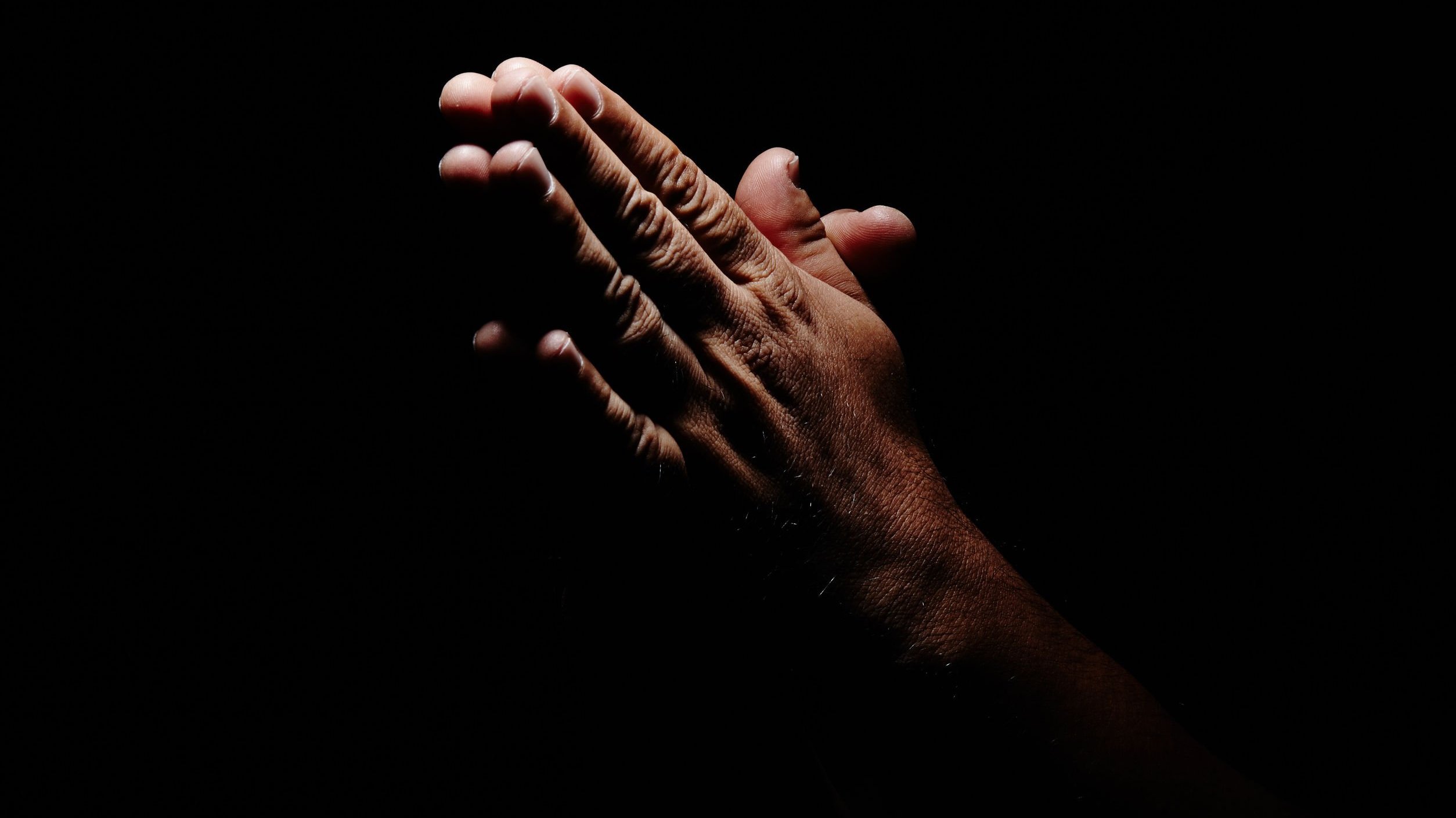 Mão de pessoa orando em frente de fundo preto