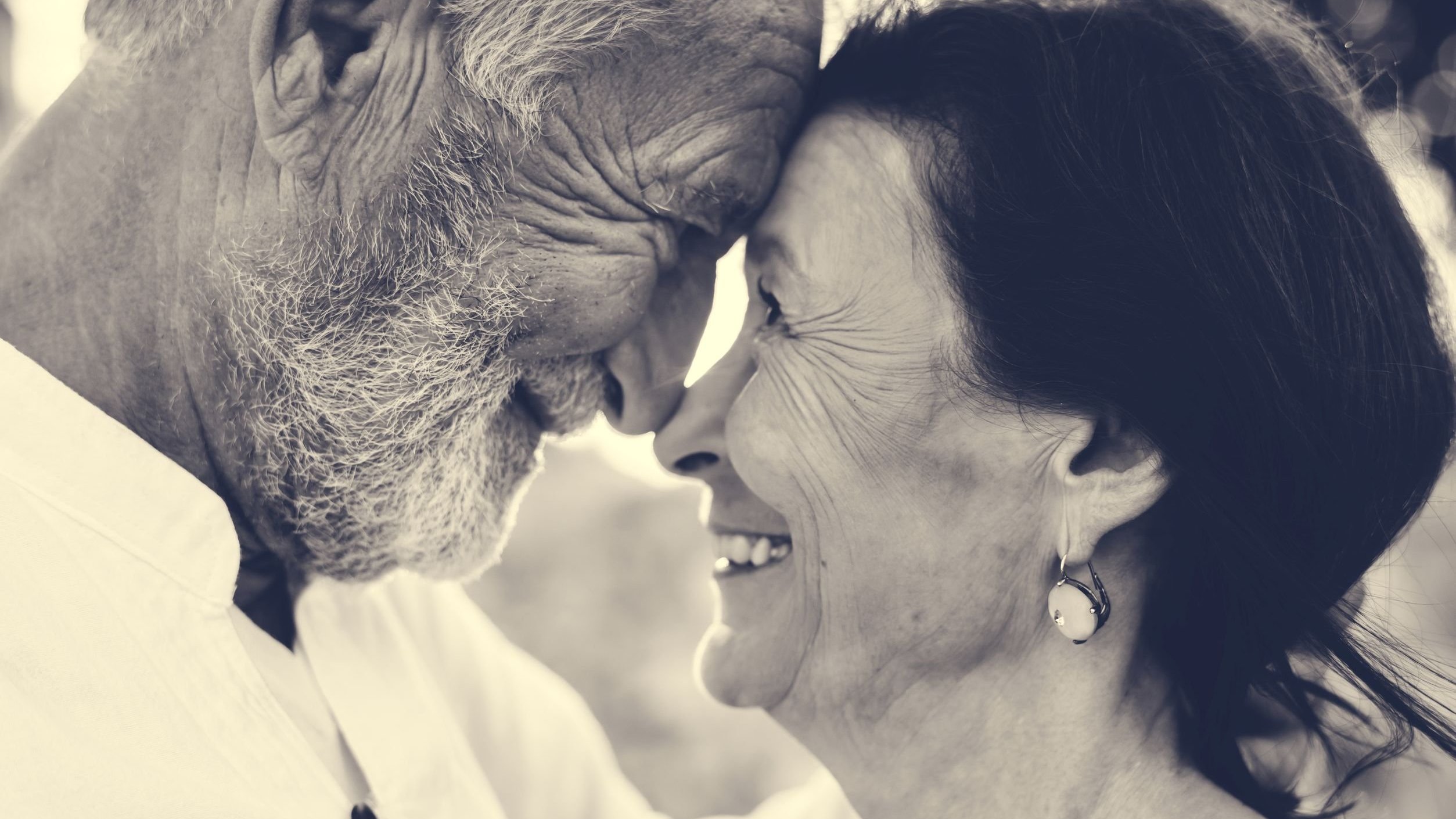 Casal de idosos sorrindo com o rosto um próximo do outro