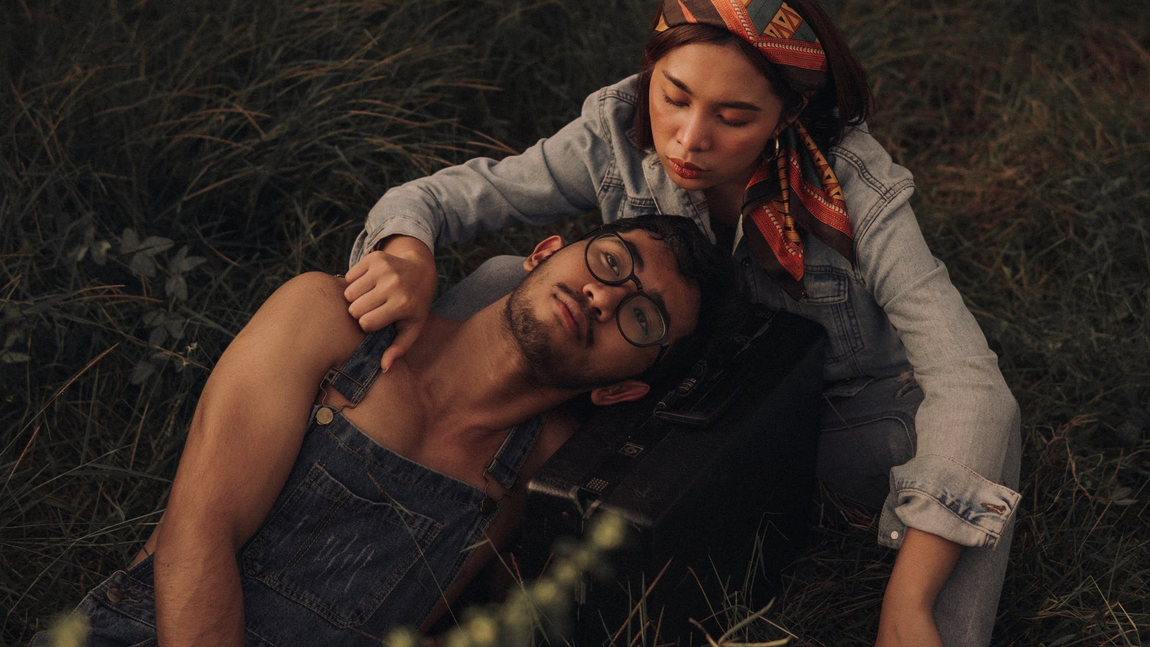 Homem deitado em grama, com mulher fazendo carinho no seu ombro