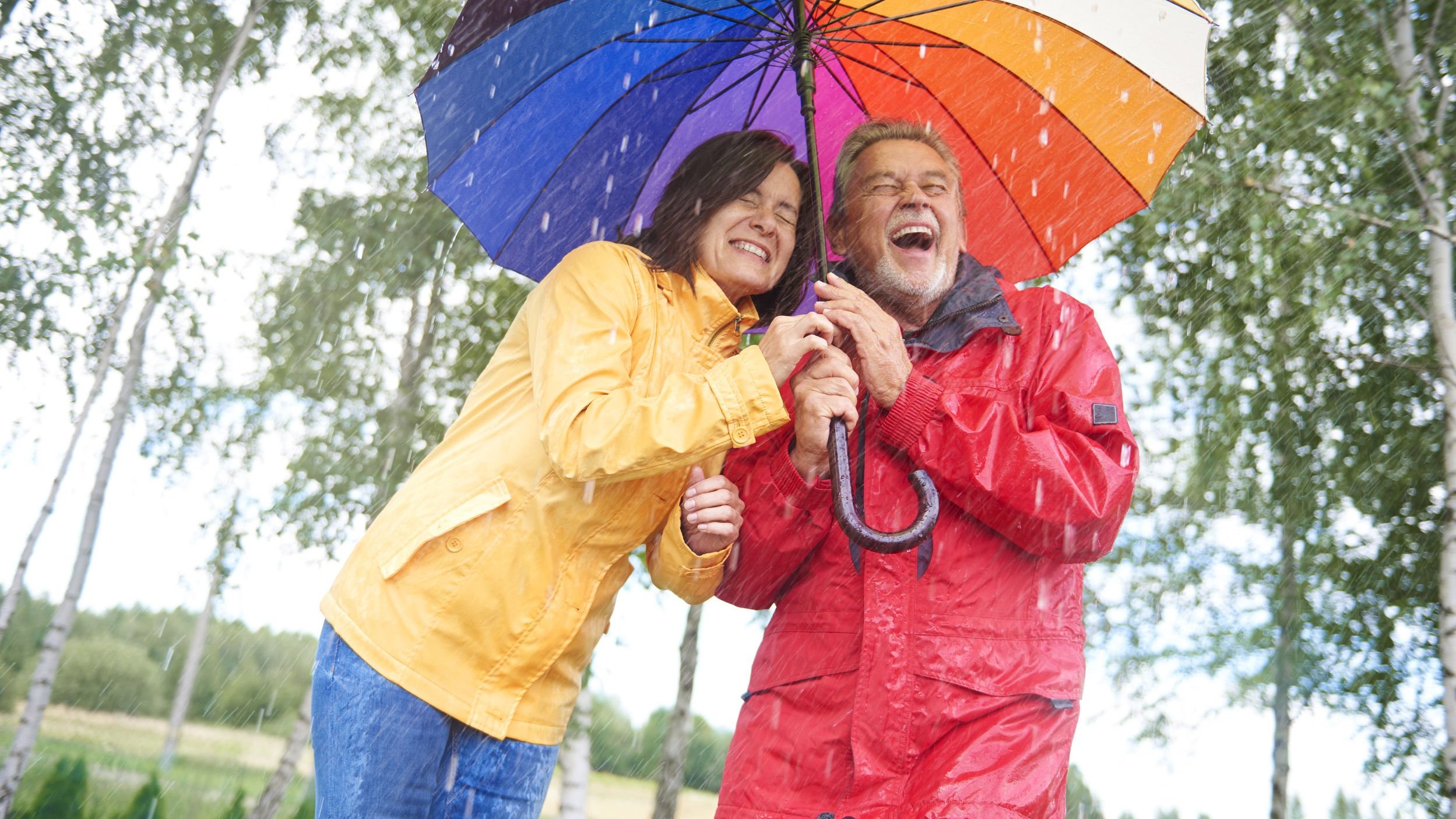 Casal abraçado dando risada ambos embaixo de um mesmo guarda chuva
