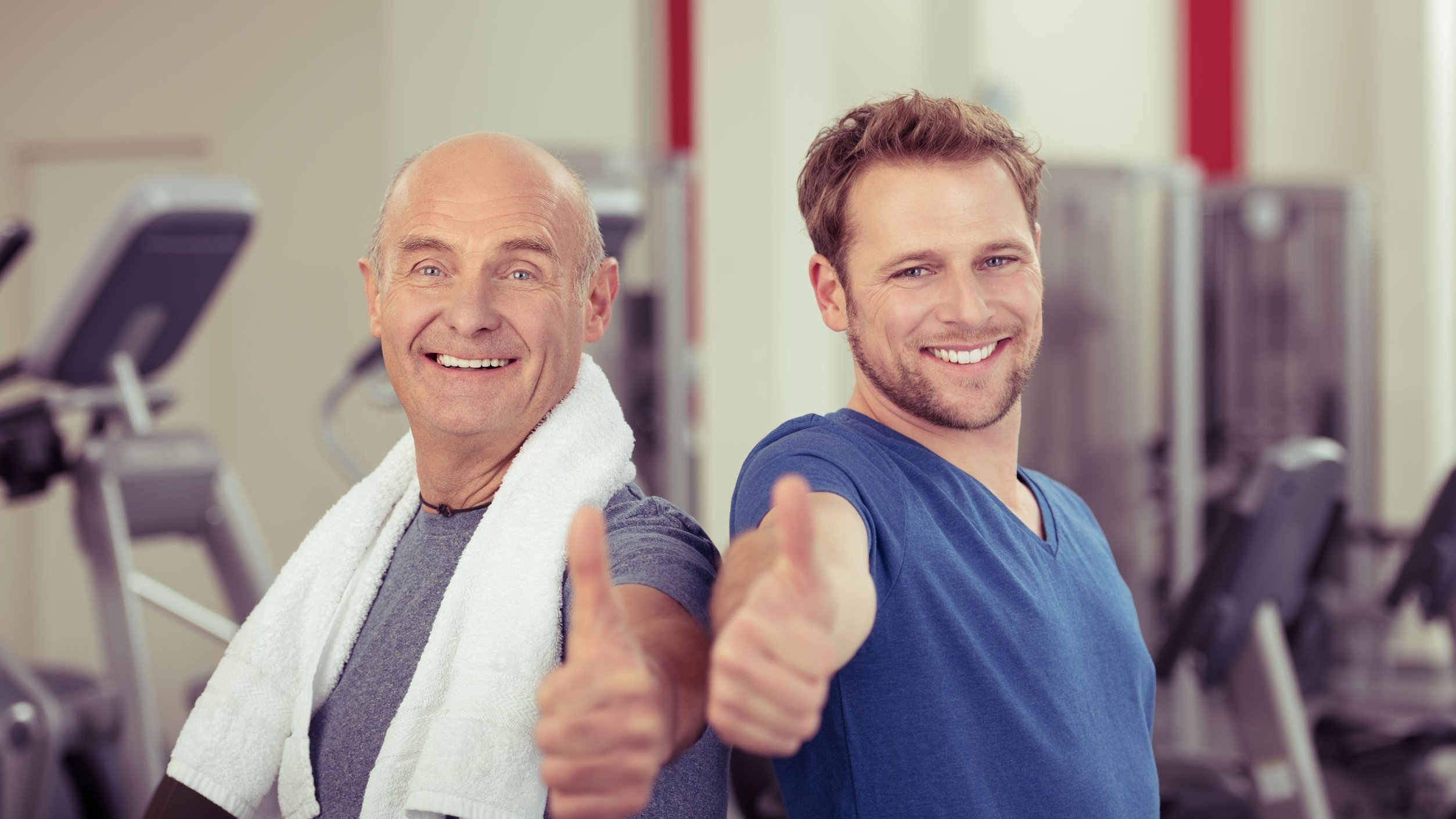 Dois homens, um jovem e um idoso, ambos sorrindo em academia