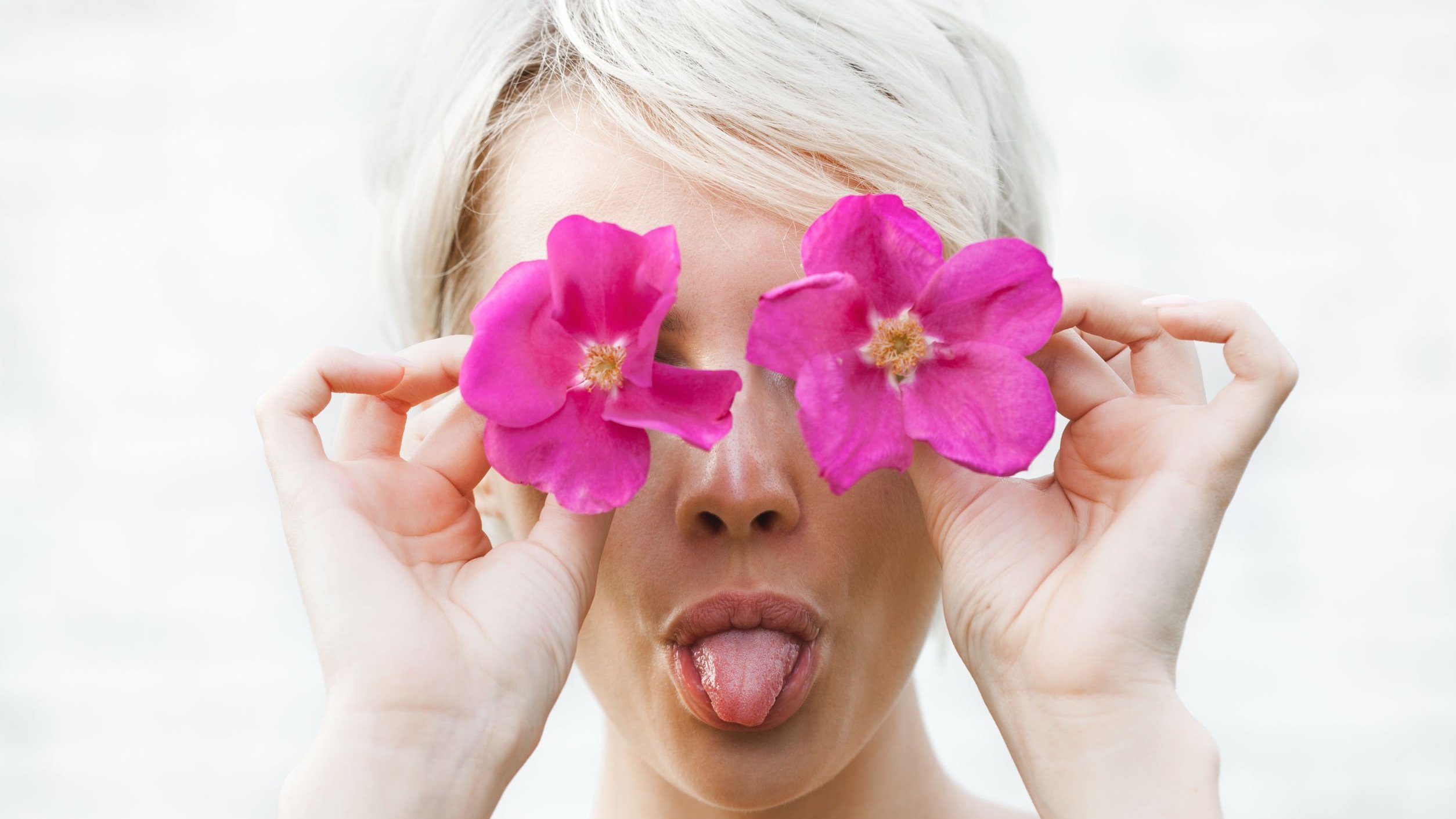 Mulher branca segurando flores rosas em frente aos olhos.