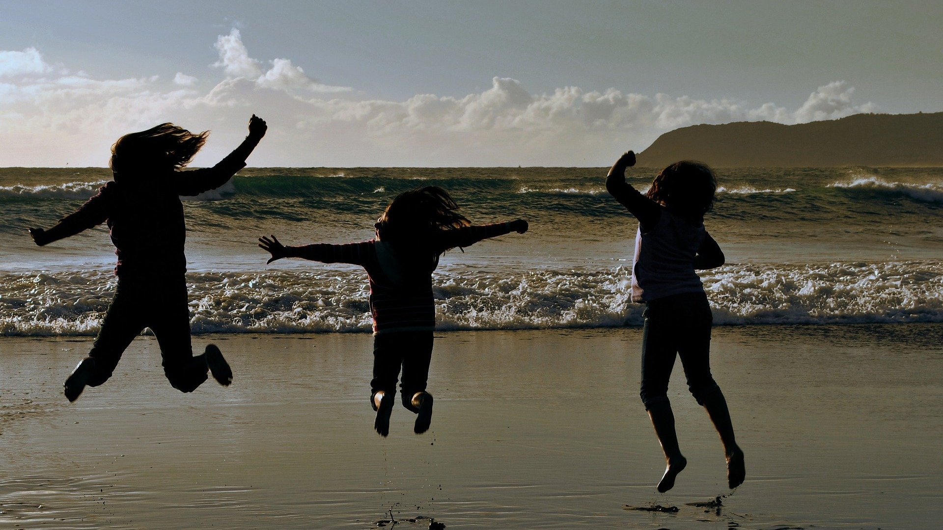 Silhueta de três pessoas pulando em praia
