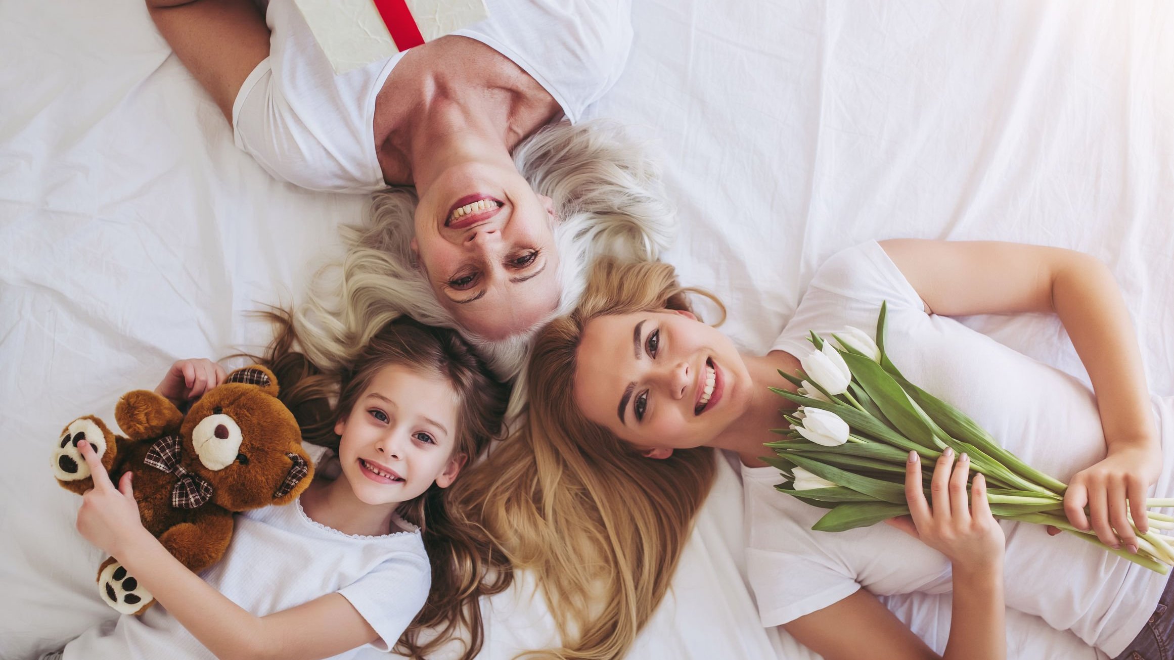 Vasyl Dolmatov /123RF Mulheres de idades diferentes, deitadas sorrindo segurando flores e bichos de pelúcia