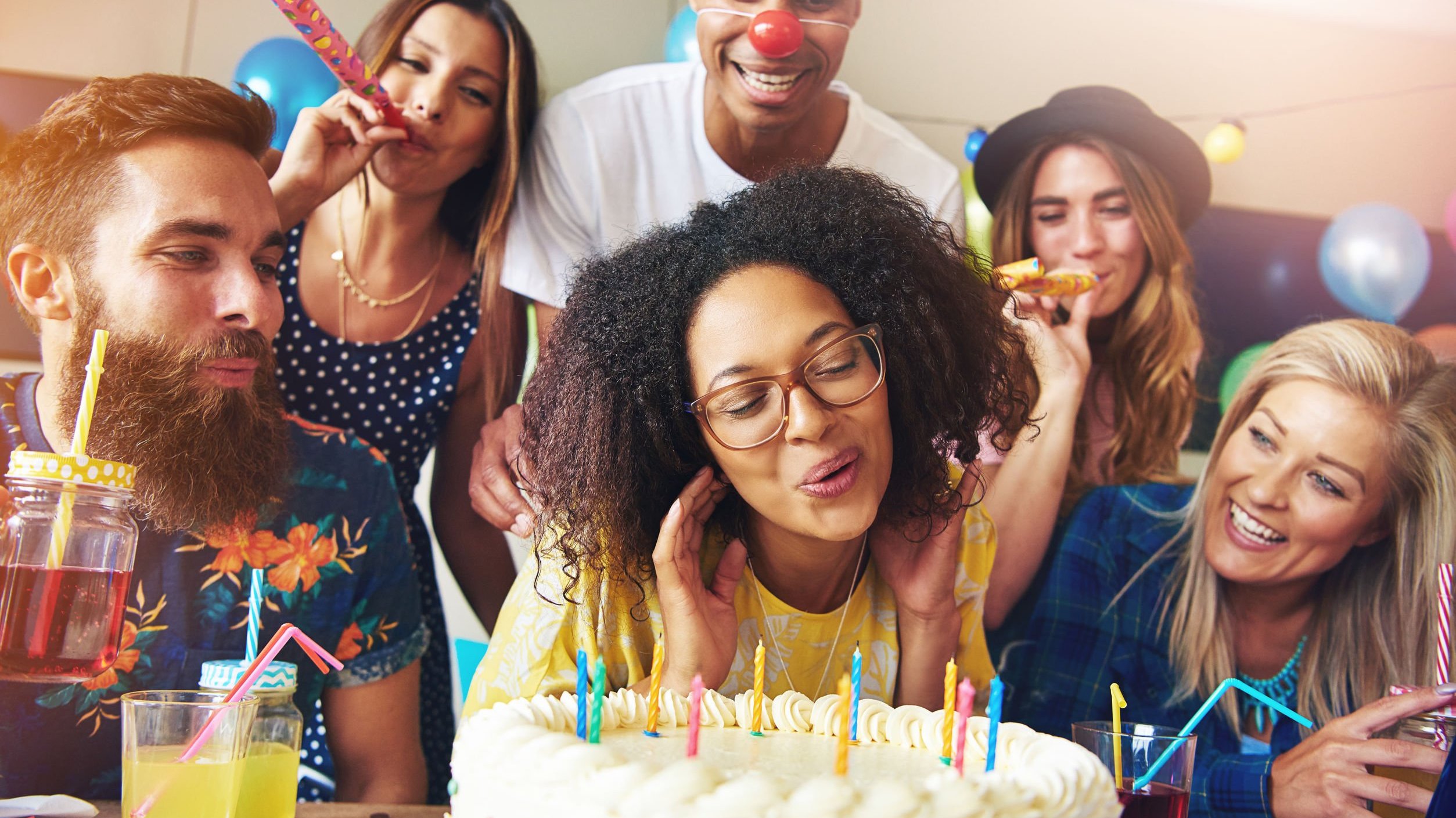 Pessoas cantando parabéns e mulher assoprando velinha acessa em cima de bolo de aniversário