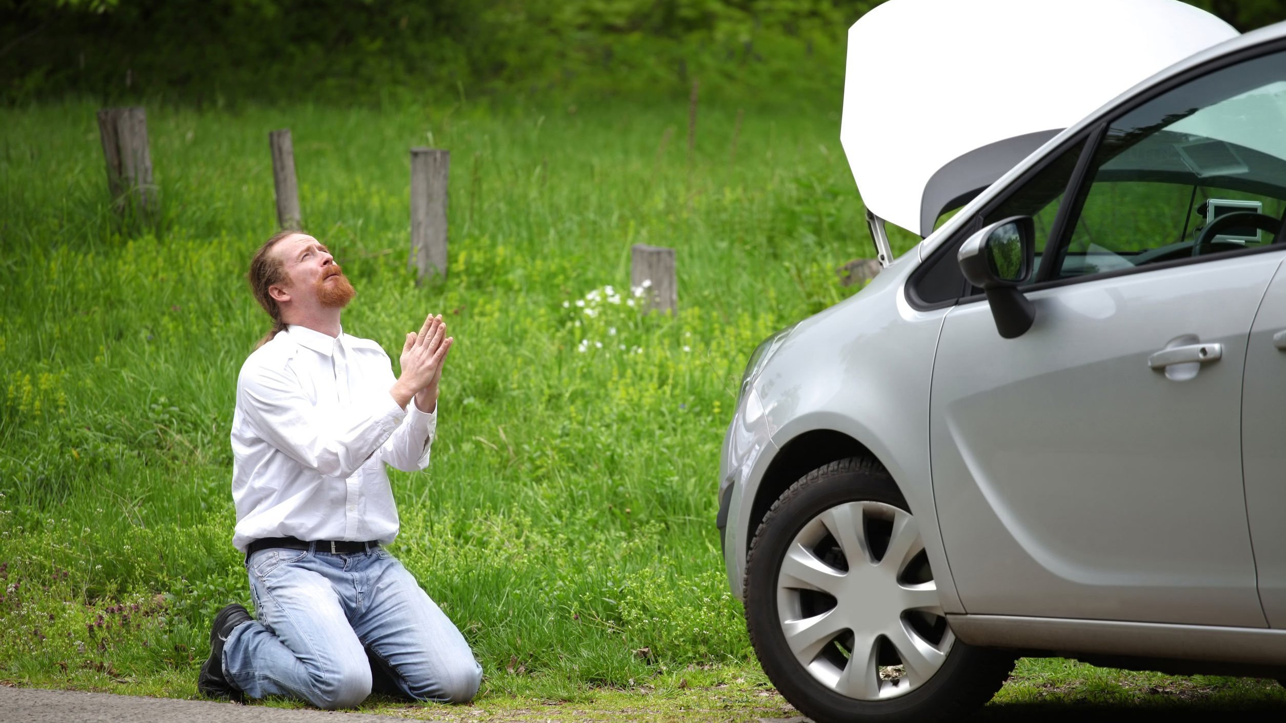 Homem ajoelhado orando em frente a carro quebrado na estrada