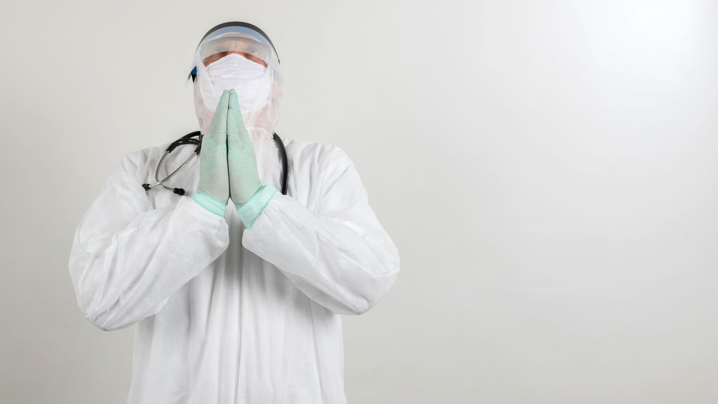 Médico usando equipamento de proteção orando com as mãos juntas