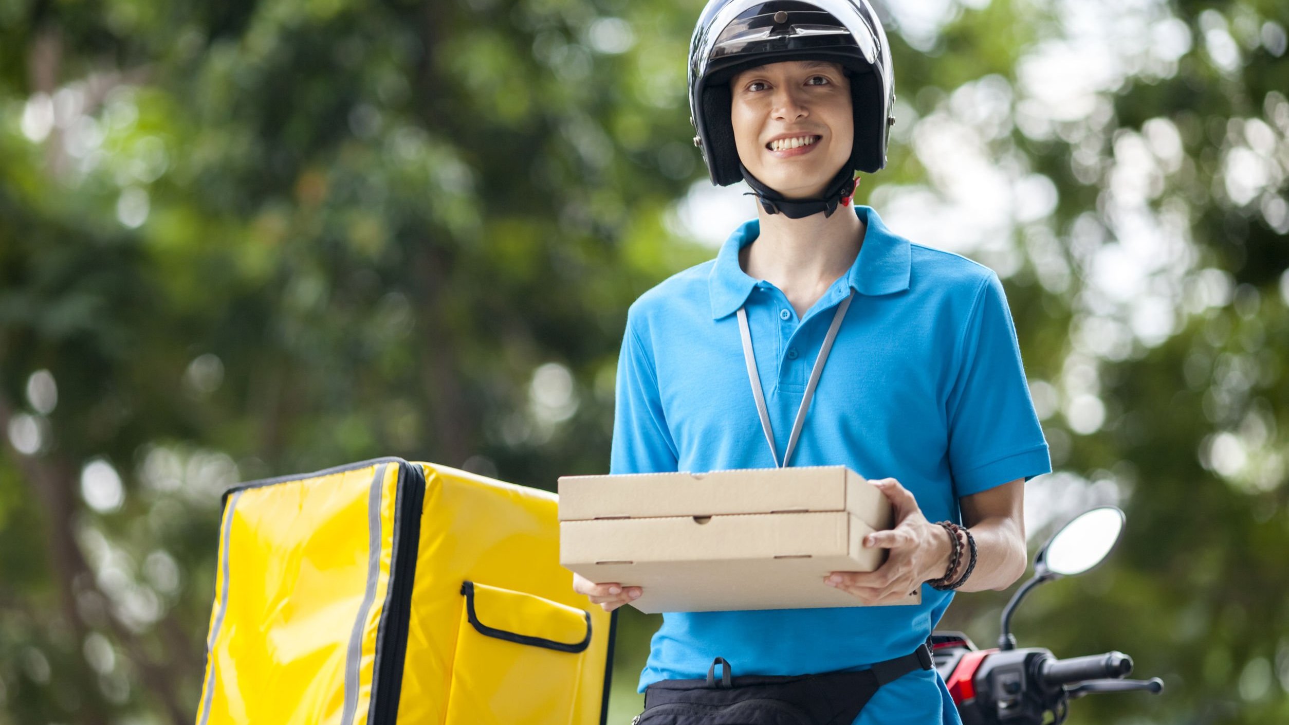 Homem segurando caixas de pizza em pé ao lado de moto, sorrindo
