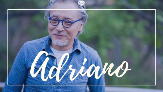 Nome Adriano escrito em branco sobre foto de homem de meia idade, asiático, usando óculos de grau e camisa social, ambos na cor azul.