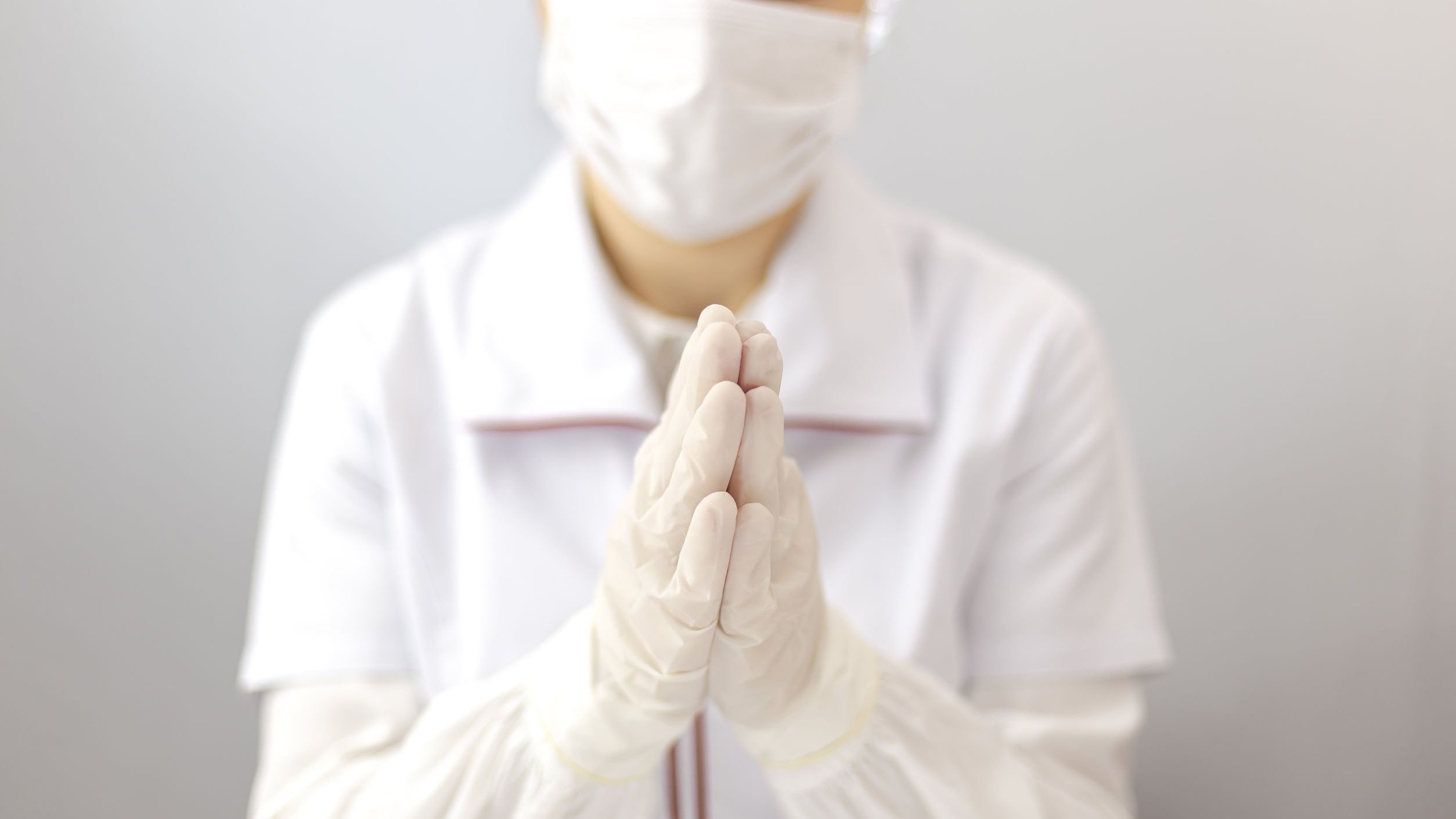 Enfermeiro usando equipamento de proteção, com as mãos juntas orando