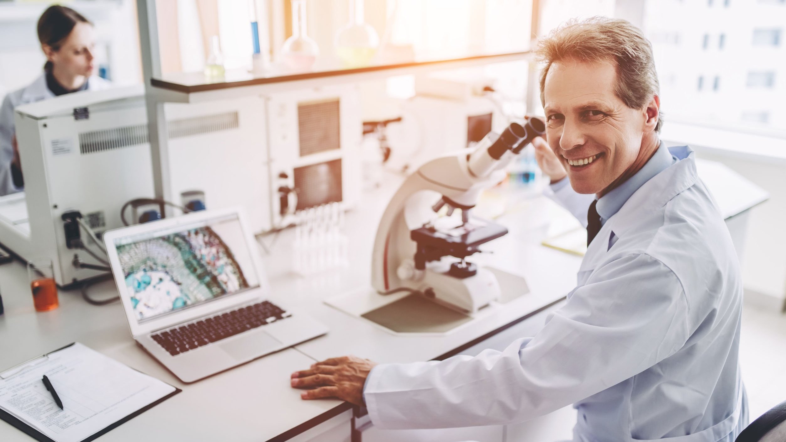 Cientista homem sorrindo, sentado em balcão de laboratório