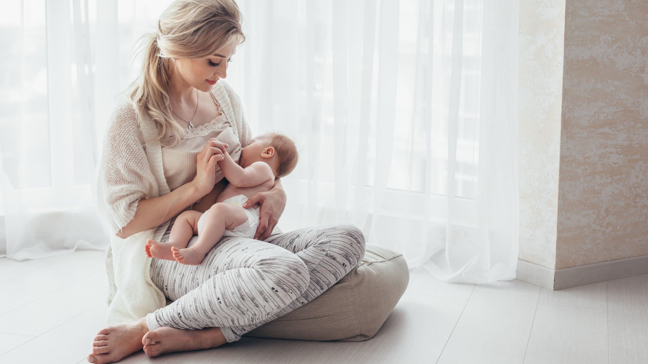 Mulher amamentando bebê sentada em almofada no chão