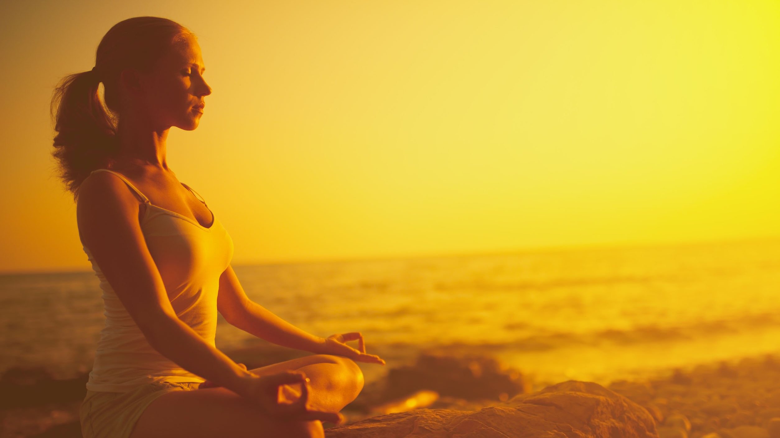 Evgeny Atamanenko/123RF Mulher sentada de pernas cruzadas e olhos fechados meditando na praia