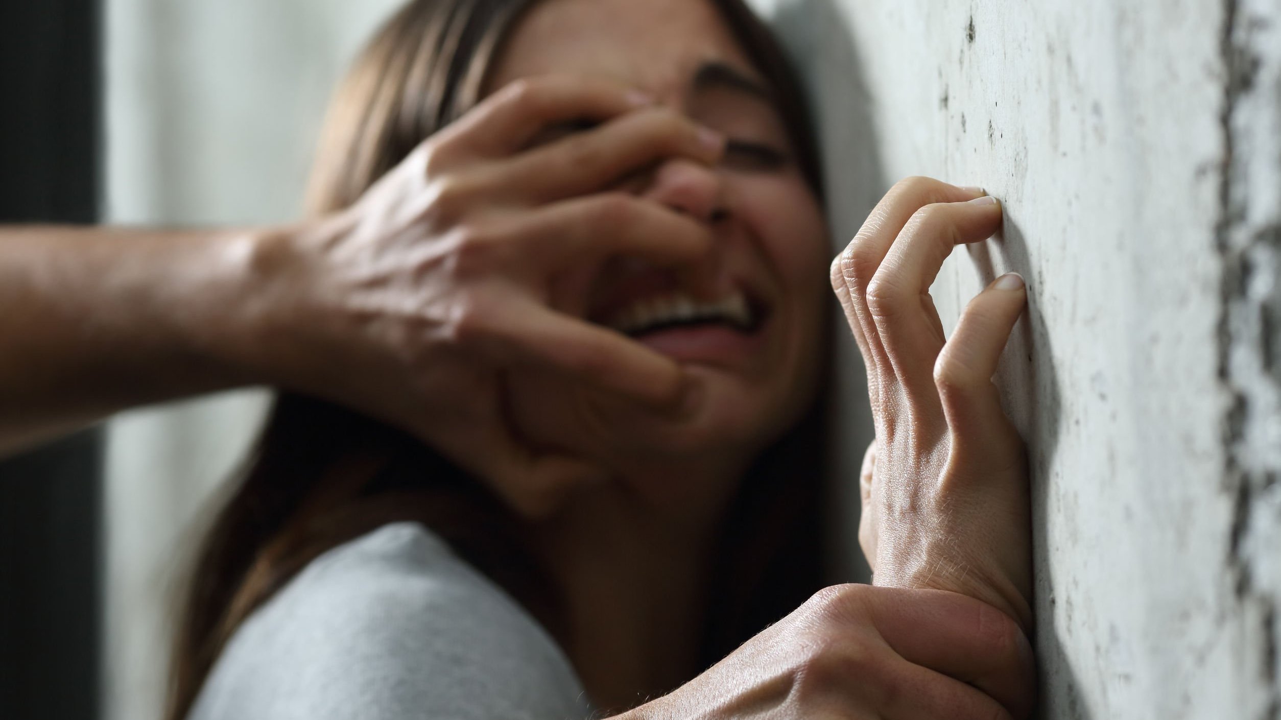 Mão de homem empurrando rosto de mulher chorando contra parede