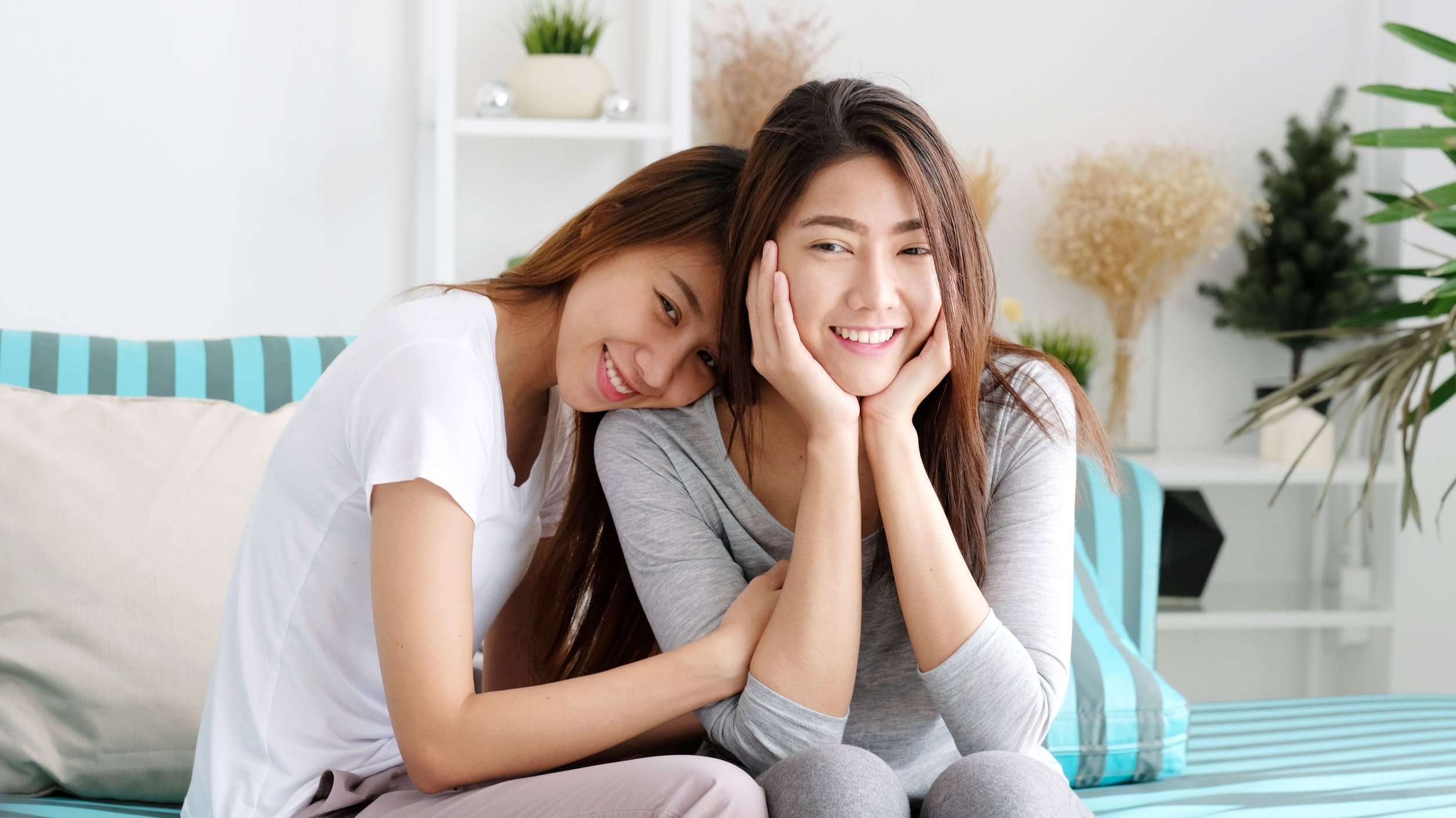 Amigas sorrindo e se abraçando, ambas sentadas em sofá