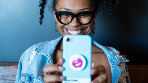 Mulher sorrindo segurando celular em direção ao rosto