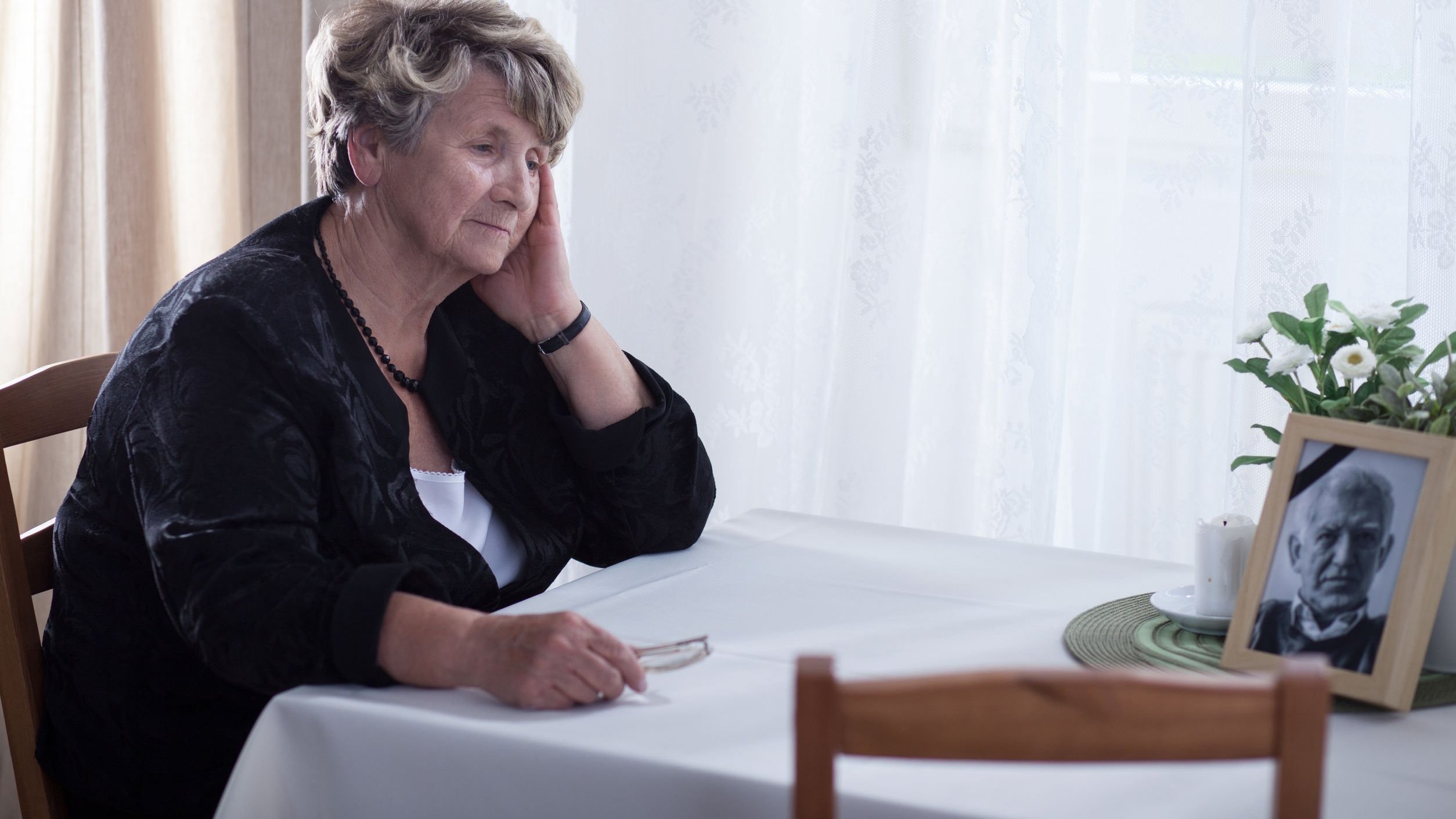 Senhora de idade sentada em mesa observando foto de homem falecido