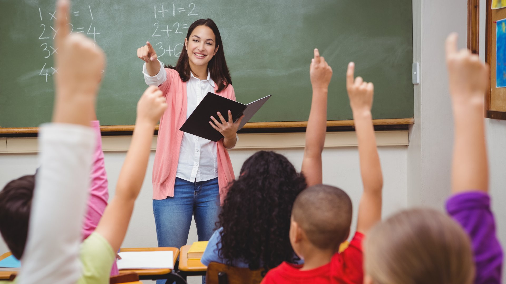 Pedagoga dando aula para crianças que estão com as mãos levantadas