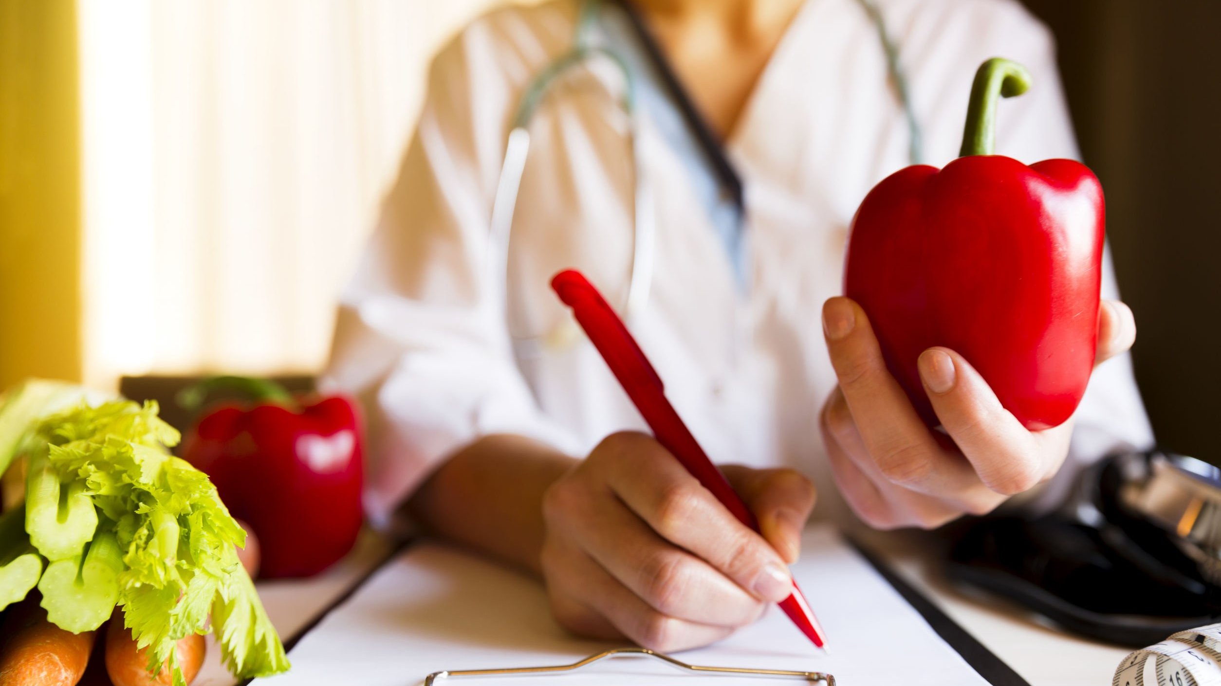 Nutricionista segurando um pimentão e fazendo anotações